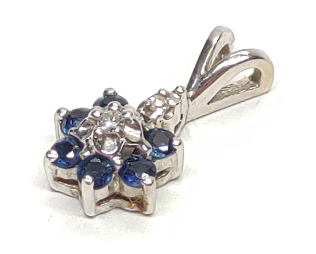 14K White Gold Diamond & Sapphire Flower Pendant: 14 karat white gold sapphire and diamond flower necklace pendant. Features 6 round cut 0.36ctw blue sapphires and two round diamond accents, clustered into a flower setting. Backside is marked "14K" w