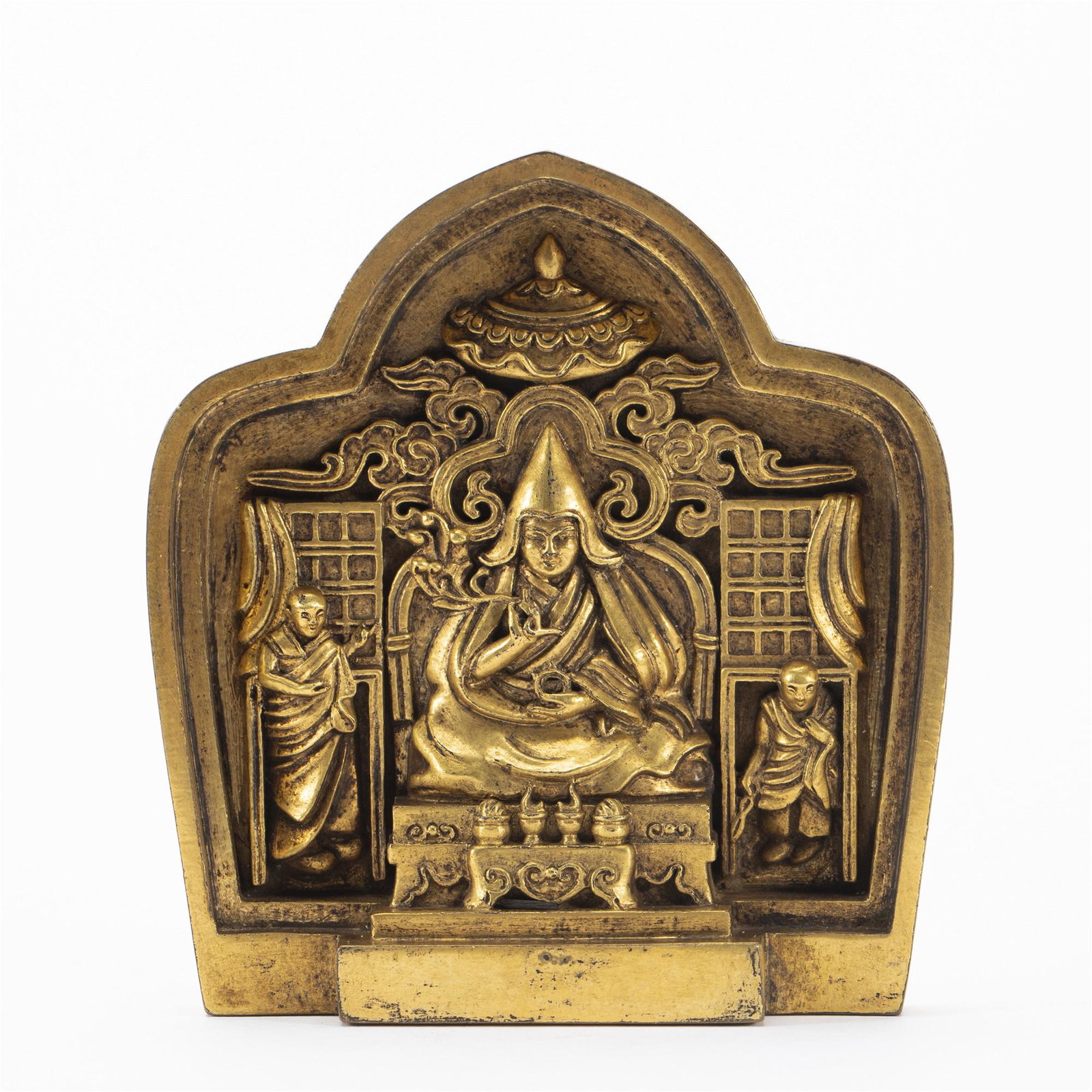 A TIBETAN BRONZE-GILT FRIEZE OF MASTER: A TIBETAN BRONZE-GILT FRIEZE OF MASTER The center deity seated on a cushion, the right hand raised in vitarkamudra and the left held in the lap, dressed in heavy robes, with a lotus blossom at right s