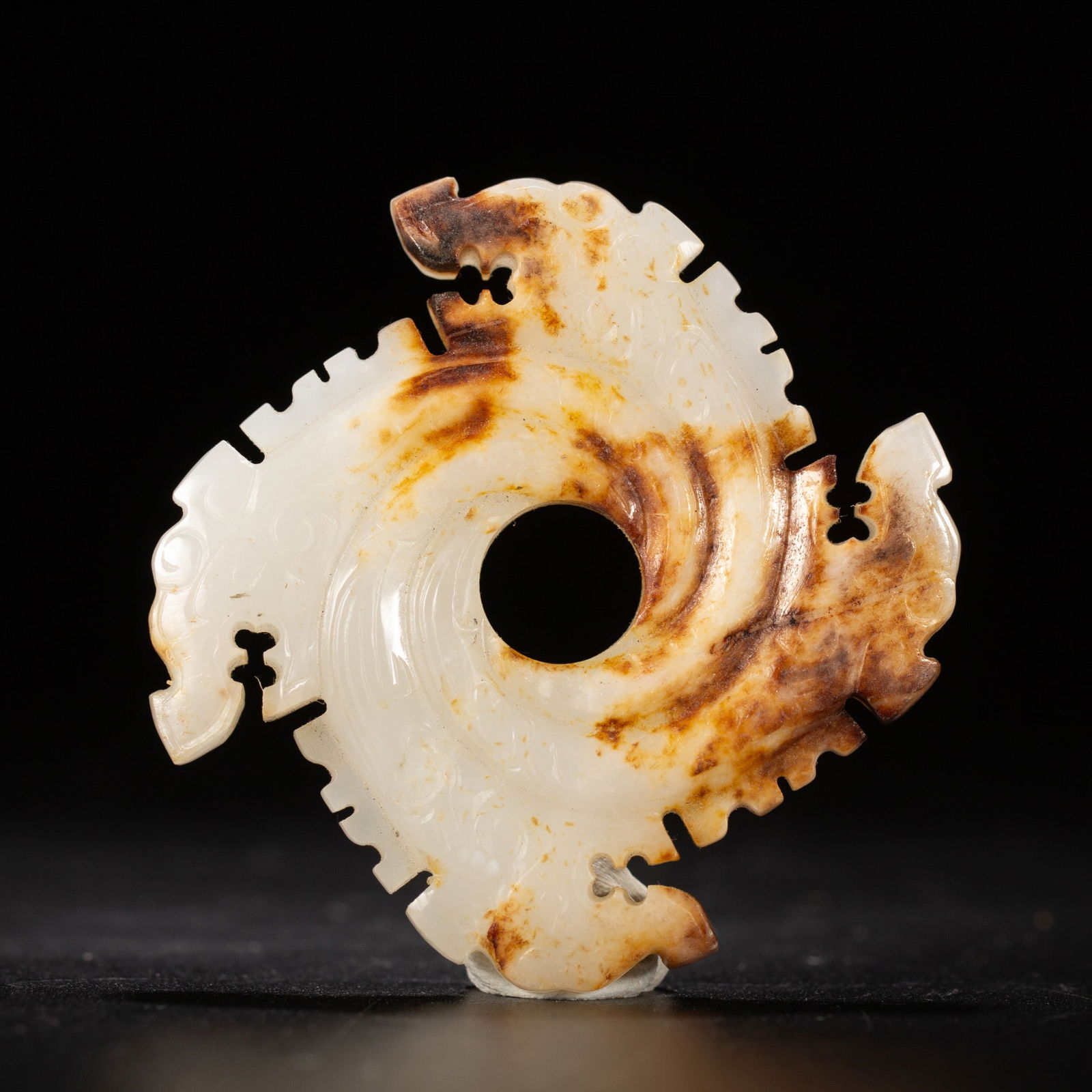 A JADE CARVING OF NOTCHED DISC XUANJI: A JADE CARVING OF NOTCHED DISC XUANJI With four deeply cut notches forming three arcs, each set with pronged teeth, the stone is of white tone with russet speckles. DIMENSIONS: L. 5 cm. W. 5 cm. Weigh