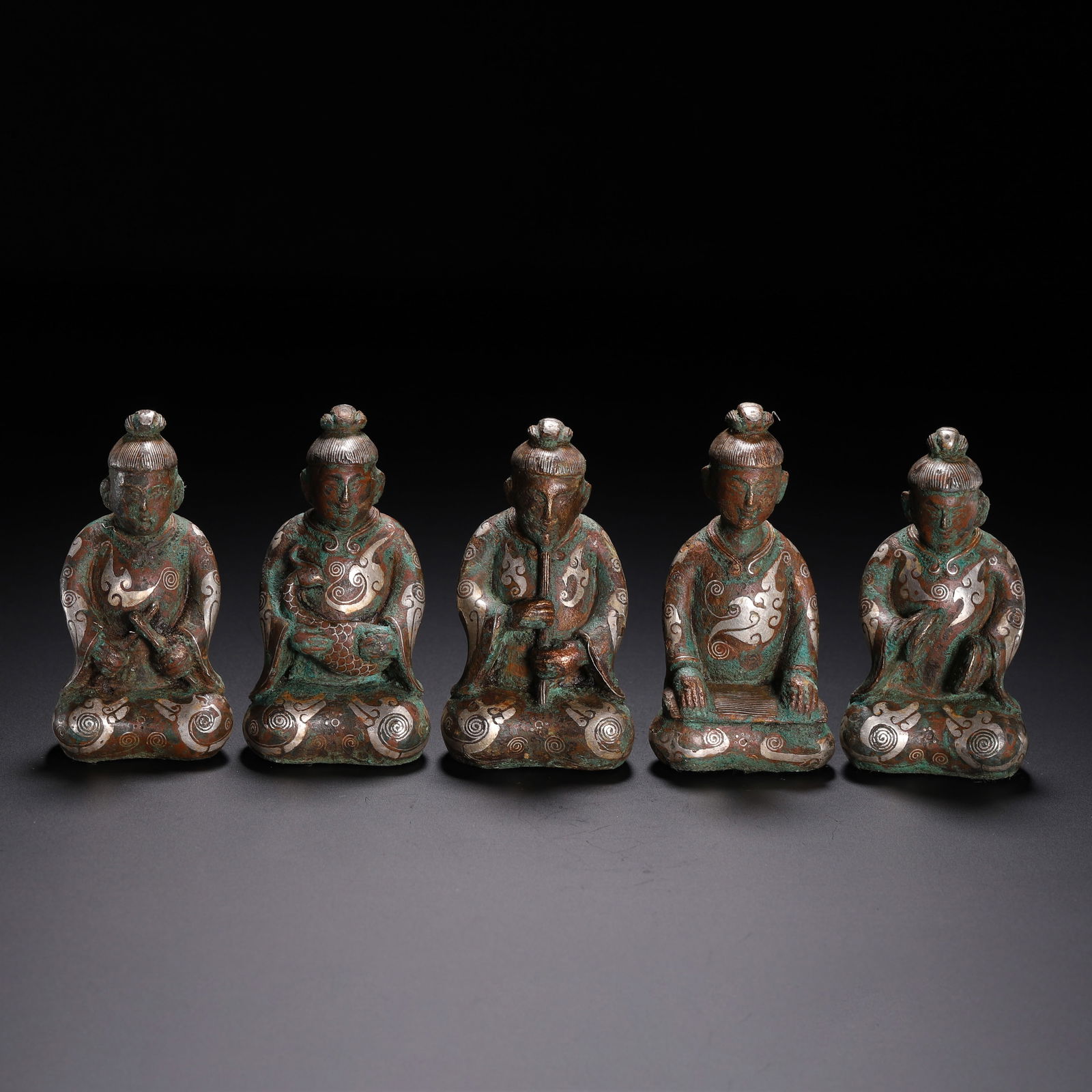 A GROUP OF SILVER INLAID KNEELING FIGURES: A GROUP OF SILVER INLAID KNEELING FIGURES This set of five seated figures is cast in bronze, each depicted in a kneeling posture, engaged in different musical or ceremonial activities—holding a flut