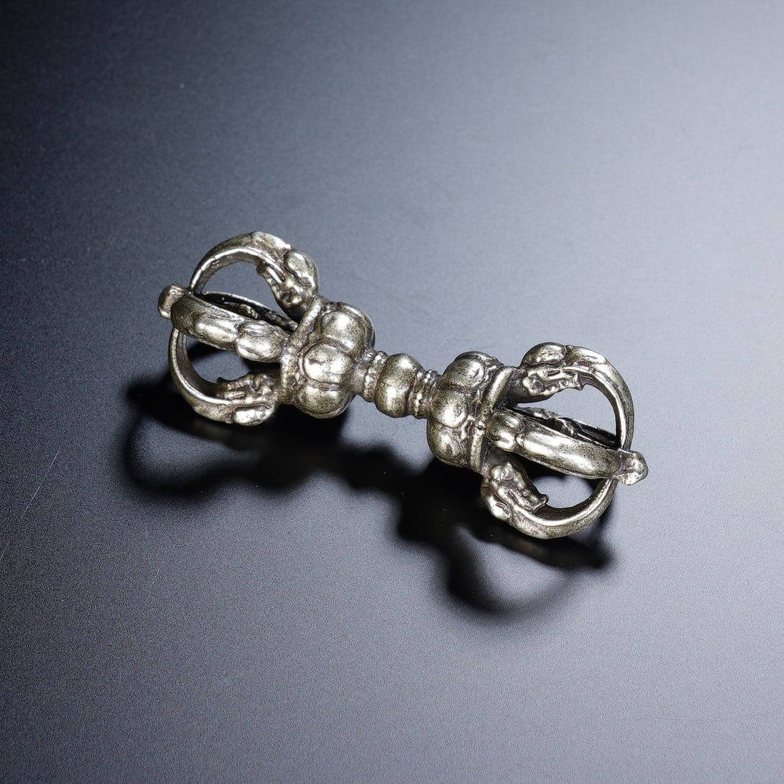 A TIBETAN BRONZE VAJRA: A TIBETAN BRONZE VAJRA A powerful Tibetan Buddhist ritual implement, this bronze vajra pestle features a classic nine-pronged design, with intricate, interlocking details on both ends. The surface bea