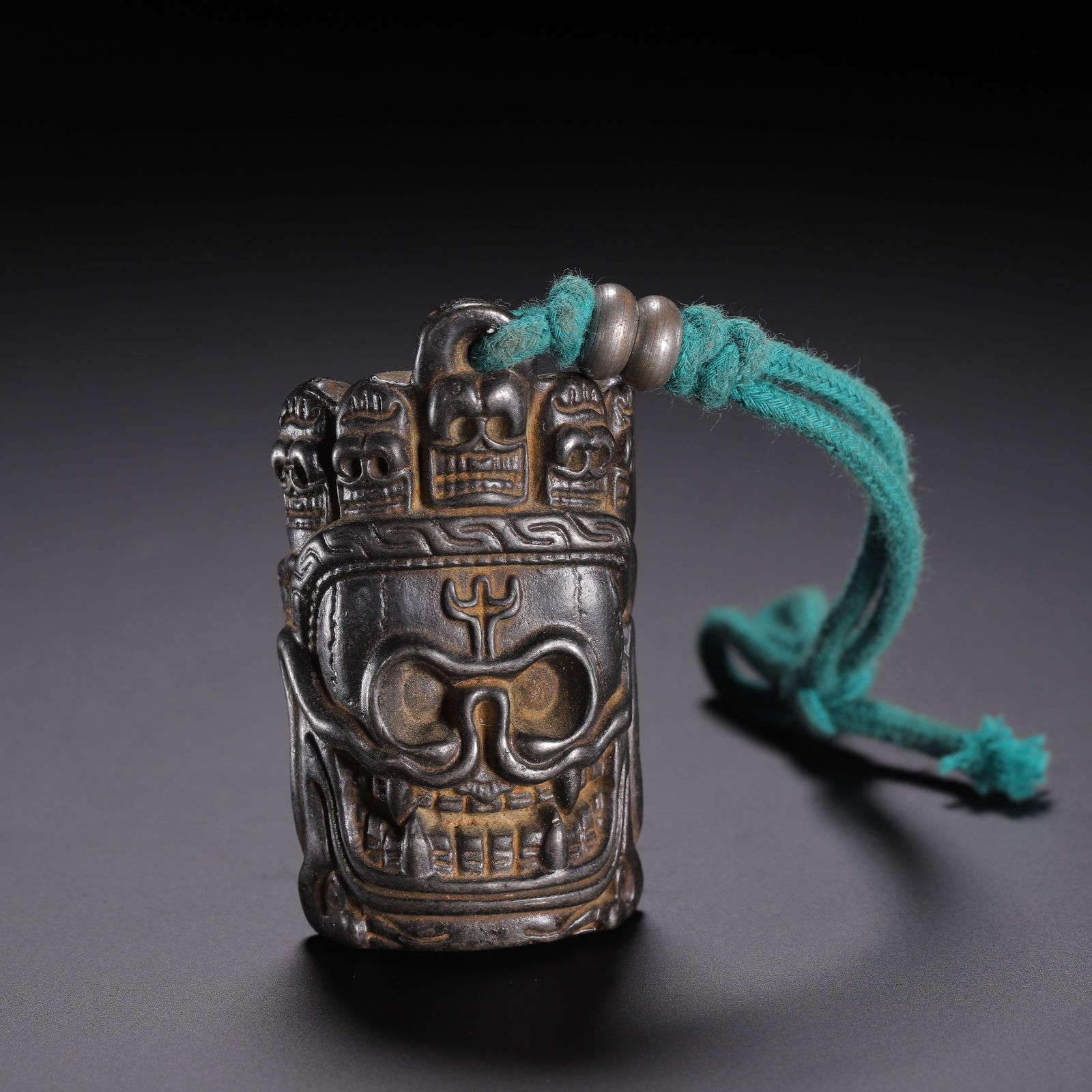 A TIBETAN BRONZE PENDANT: A TIBETAN BRONZE PENDANT This Tibetan copper pendant is deeply carved in relief with a fierce Citipati skull, flanked by smaller skulls along the top edge. The surface displays a rich dark patina