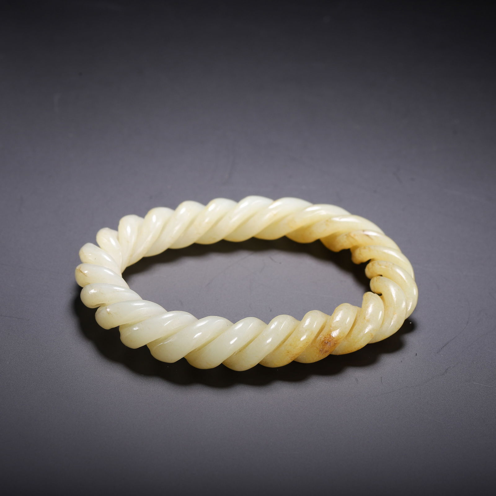 A WHITE JADE BANGLE: A WHITE JADE BANGLE This elegant Chinese bangle is carved from pale celadon Hetian jade, featuring a continuous twisted rope design. The stone exhibits a smooth, polished surface with a soft, waxy