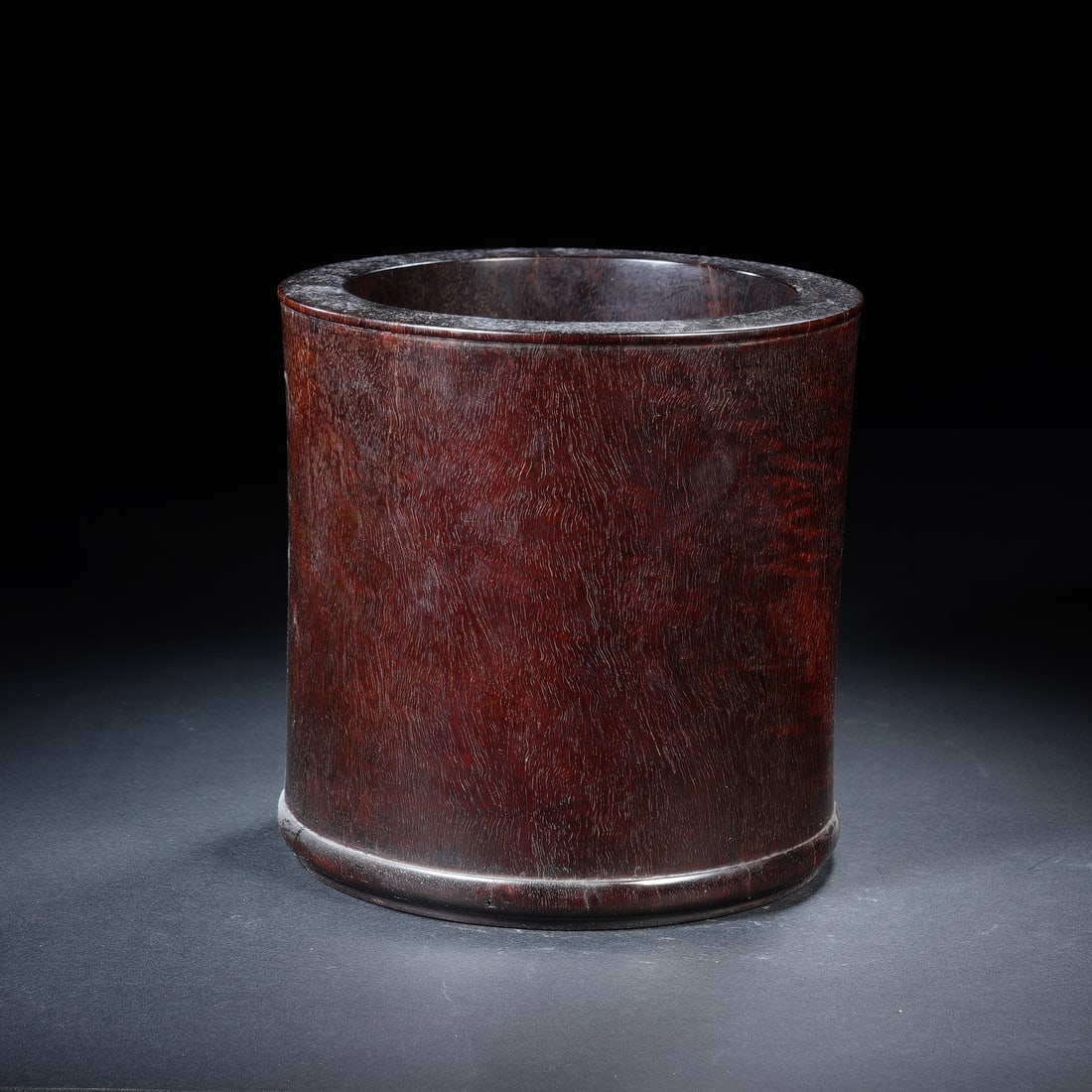A ROSEWOOD ZITAN BRUSHPOT: A ROSEWOOD ZITAN BRUSHPOT A refined Chinese brush pot, expertly carved from a single piece of dense, lustrous zitan wood. Its elegant cylindrical form features subtle raised lines at the rim and