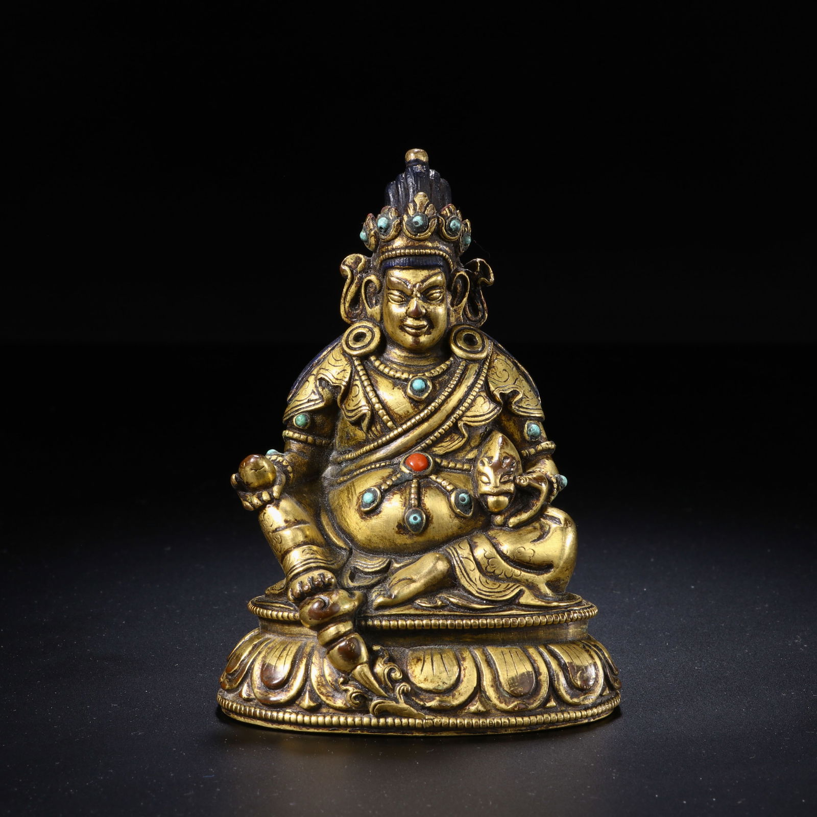 A COPPER ALLOY FIGURE OF JAMBHALA: A COPPER ALLOY FIGURE OF JAMBHALA This finely cast Chinese gilt-bronze figure depicts Jambhala, the Buddhist deity of wealth, seated in a relaxed lalitasana pose atop a double-lotus base. The