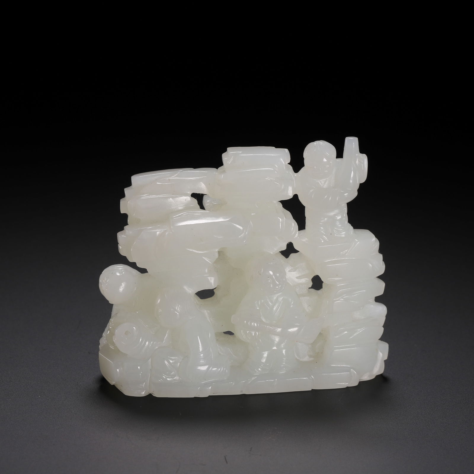 A CARVED WHITE JADE BOYS DECORATION: A CARVED WHITE JADE BOYS DECORATION This delightful carving is masterfully crafted from translucent white Hetian jade, depicting three boys amidst stacked scrolls and rockery. One boy stands atop the