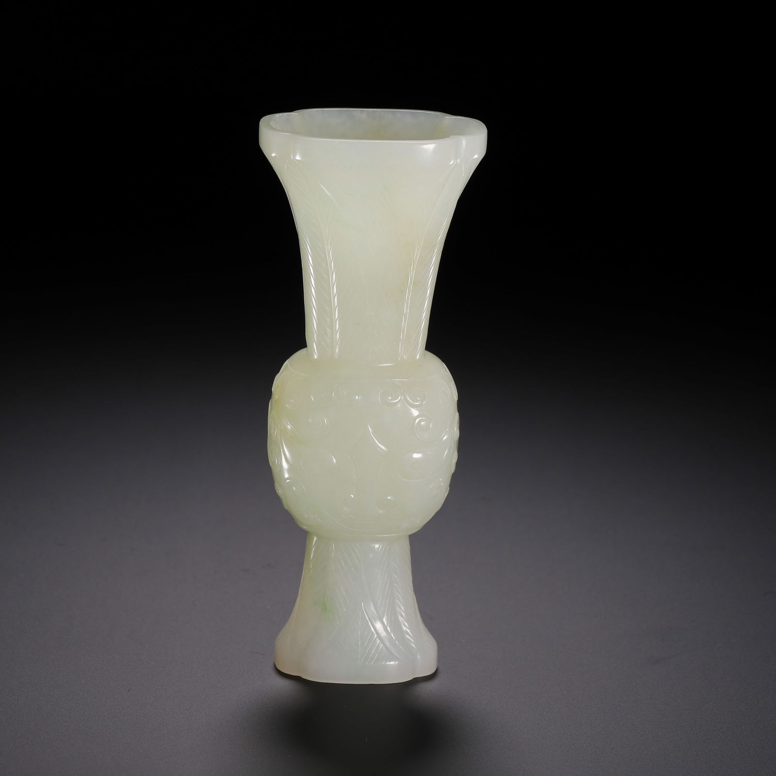 A CARVED WHITE JADE BEAKER VASE GU: A CARVED WHITE JADE BEAKER VASE GU This elegant vase is masterfully carved from a single block of pale, translucent Hetian jade, showcasing a subtle greenish hue and a smooth, lustrous finish. The for