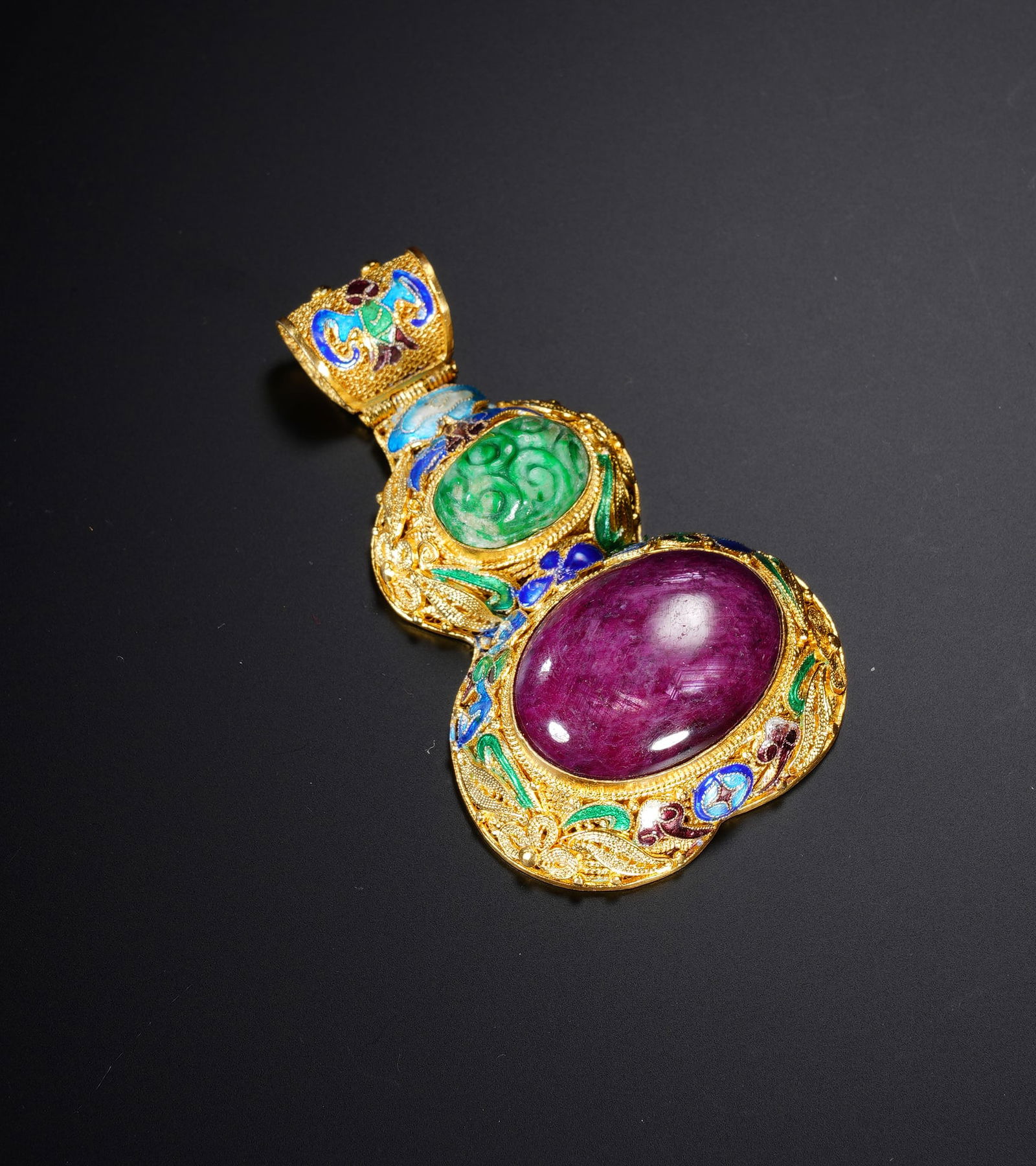 A HARDSTONES INLAID DOUBLE GOURDS PENDANT: A HARDSTONES INLAID DOUBLE GOURDS PENDANT An exceptional Chinese pendant crafted in intricate gold filigree, featuring a large, cabochon-cut ruby of rich magenta hue as its centerpiece, accented by a