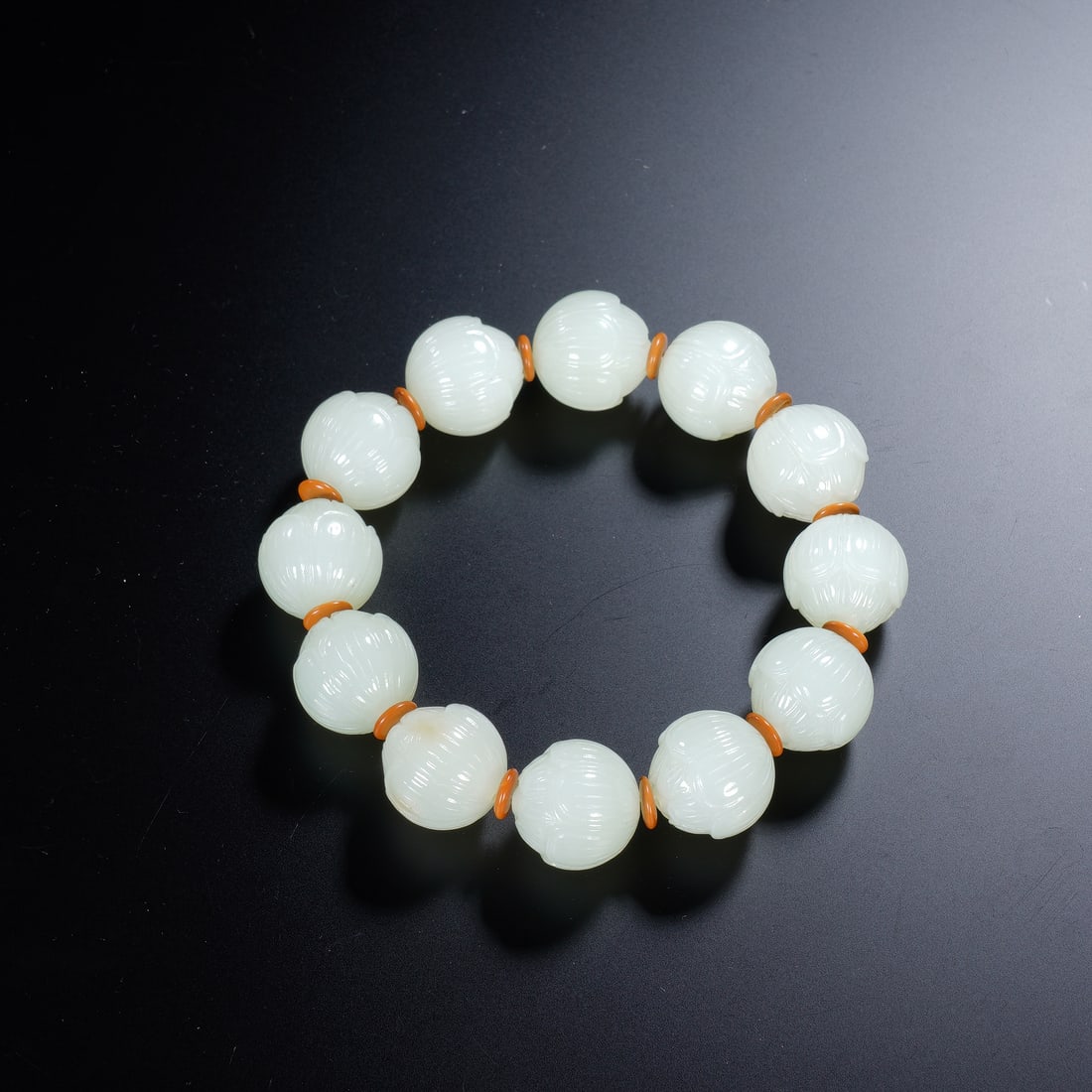 A WHITE JADE BEAD BRACELETS: A WHITE JADE BEAD BRACELETS An elegant Chinese bracelet composed of twelve carved white jade beads, each meticulously shaped into a closed lotus bud with fine, radiating petals. The beads are separate
