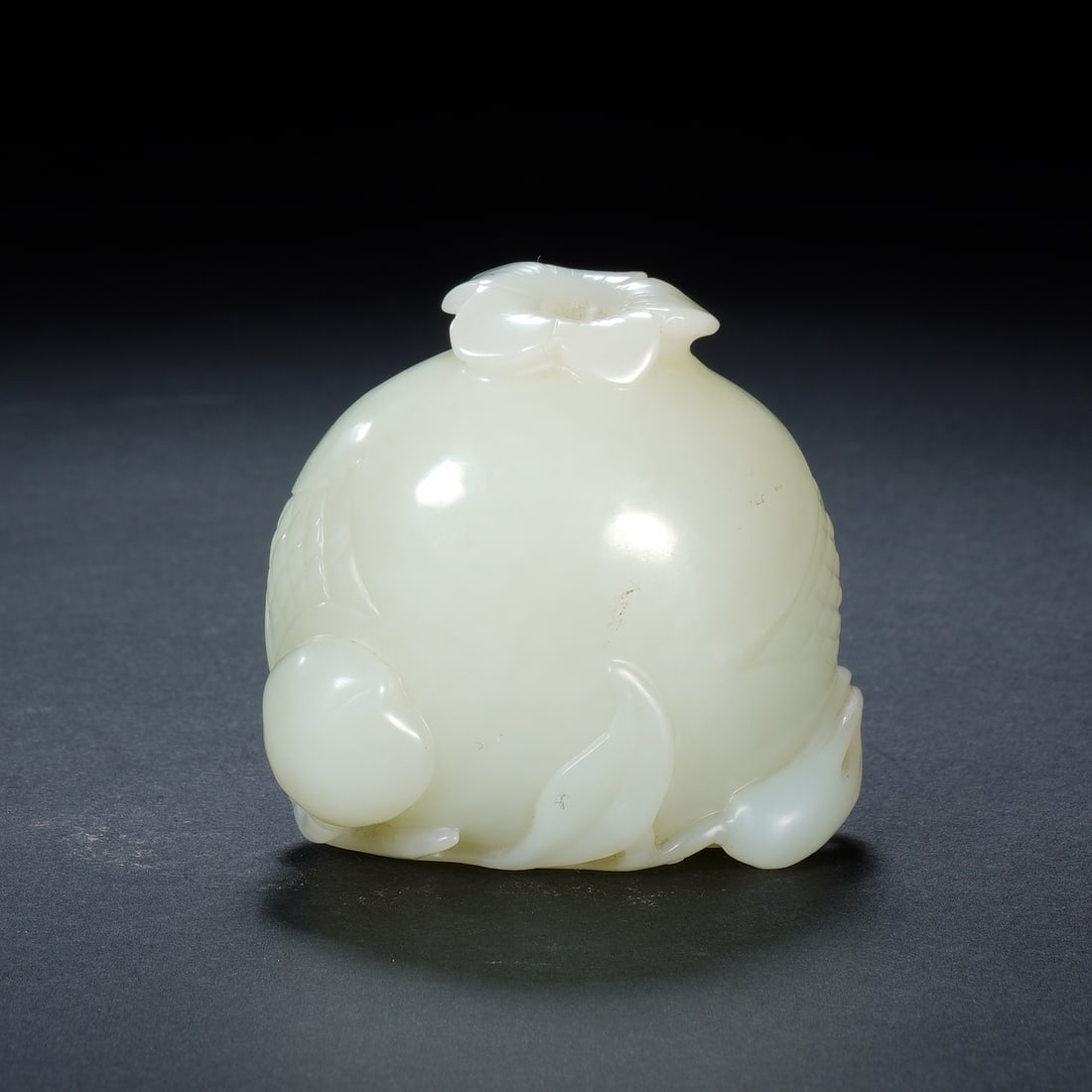 A CARVED WHITE JADE POMGRANATE: A CARVED WHITE JADE POMGRANATE A charming Chinese water dropper, expertly carved from a smooth, translucent piece of white jade. The form is a plump, naturalistic pomegranate, complete with a leafy