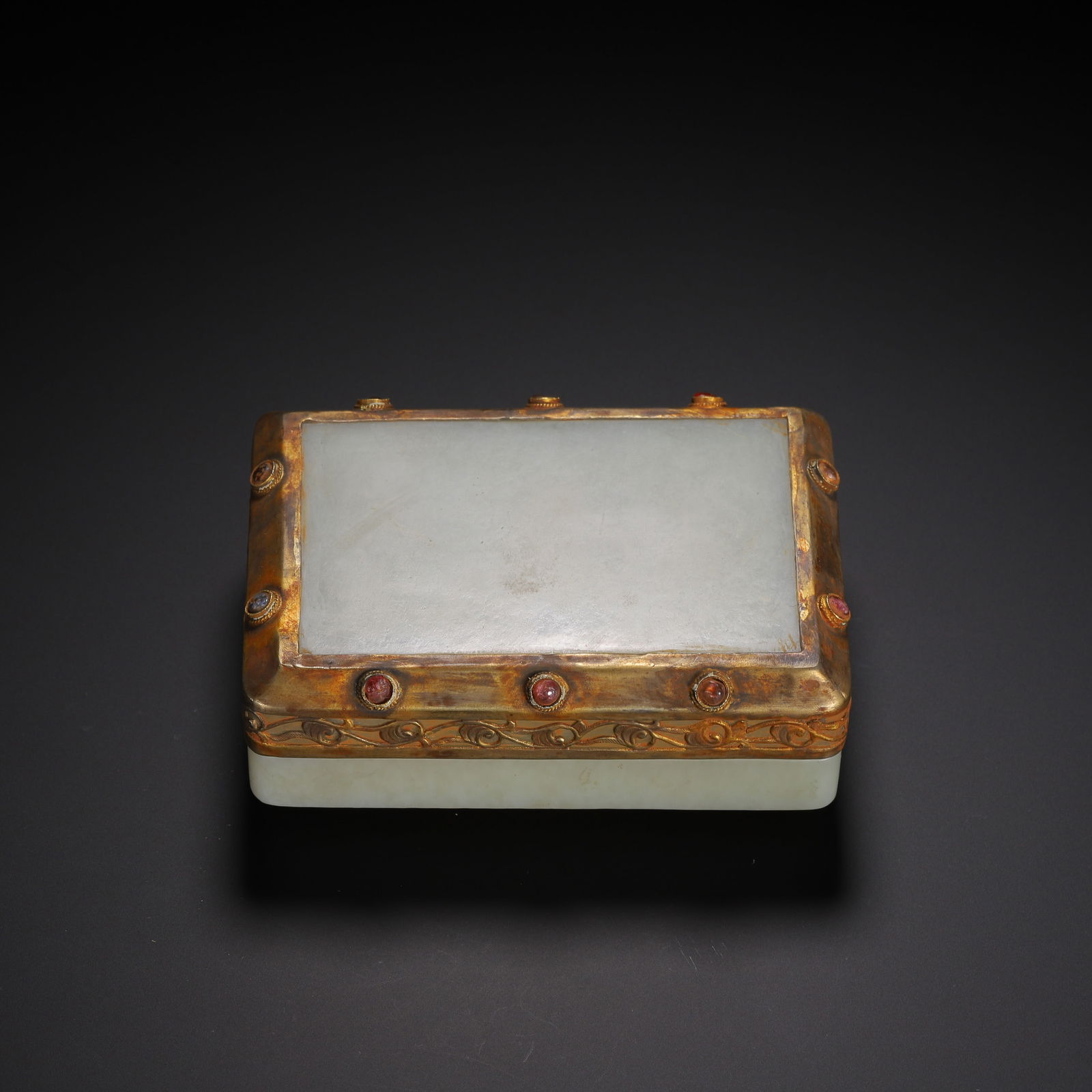 A CARVED WHITE JADE BOX WITH COVER: A CARVED WHITE JADE BOX WITH COVER This rectangular covered box is formed from pale, milky-white Hetian jade, its surface smooth and unadorned. The lid and base are encased in ornate gilt-metal mounts