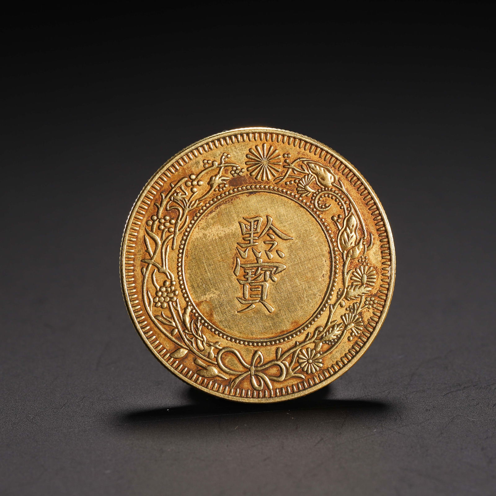 A CHINESE SILVER-GILT COIN: A CHINESE SILVER-GILT COIN This circular coin is crafted from silver and lavishly gilt, with a rich, luminous gold finish. The central field bears the characters “??” (Qian Bao), encircled by
