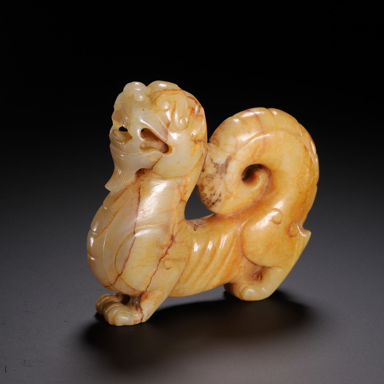 A CARVED JADE MYTHICAL BEAST: A CARVED JADE MYTHICAL BEAST This powerful Chinese archaic jade beast is carved from pale celadon jade with natural russet inclusions and prominent veining. The mythical creature is depicted in a