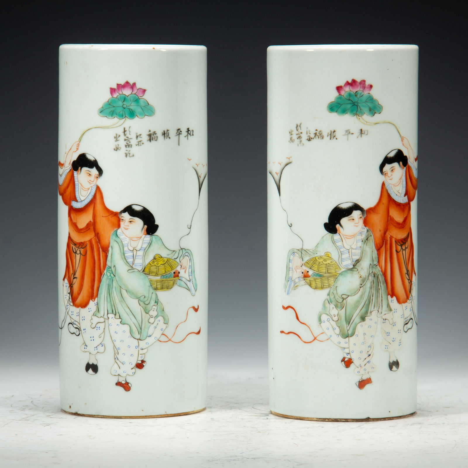 PAIR FAMILLE ROSE HAT STANDS: PAIR FAMILLE ROSE HAT STANDS This pair of Chinese porcelain hat stands is painted in vibrant famille rose enamels. Each cylindrical stand depicts the iconic Hehe Erxian (the Two Immortals of Harmony