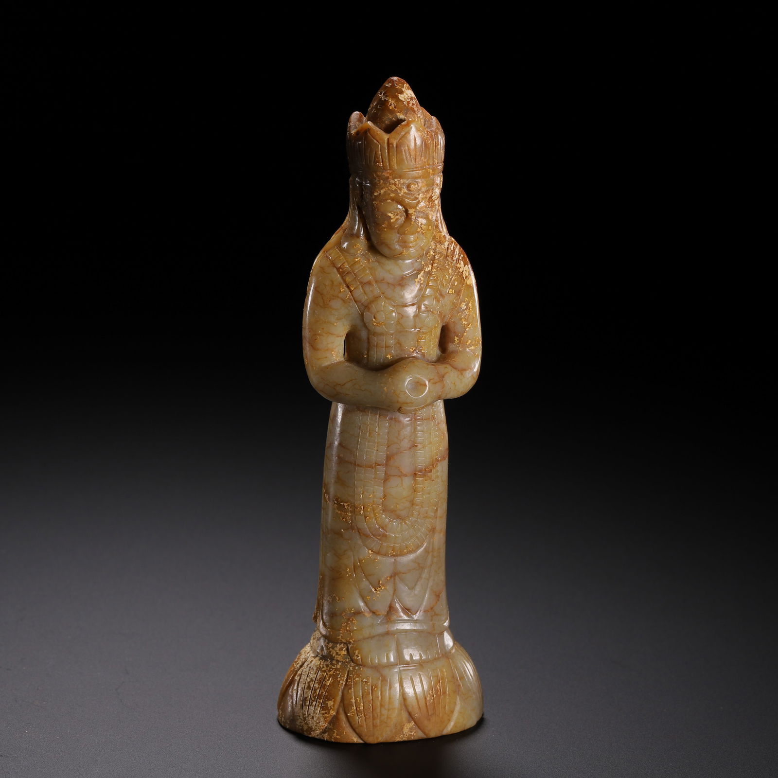 A CARVED JADE STANDING BODHISATTVA: A CARVED JADE STANDING BODHISATTVA This archaic figure is carved from pale celadon jade with prominent russet and golden-brown inclusions, exhibiting a fine network of natural veining throughout. The