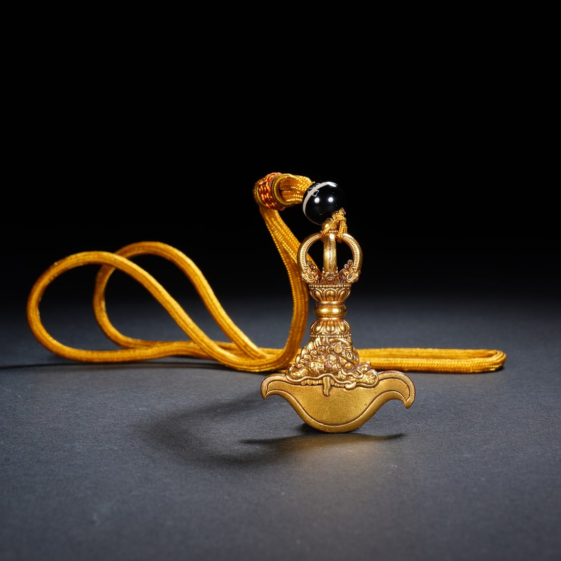 A BRONZE-GILT CURVED KNIFE: A BRONZE-GILT CURVED KNIFE A finely cast Tibetan Buddhist ritual implement, this gilt-bronze pendant depicts a vajra axe (kartika), a symbol of wisdom cutting through ignorance. The axe head is