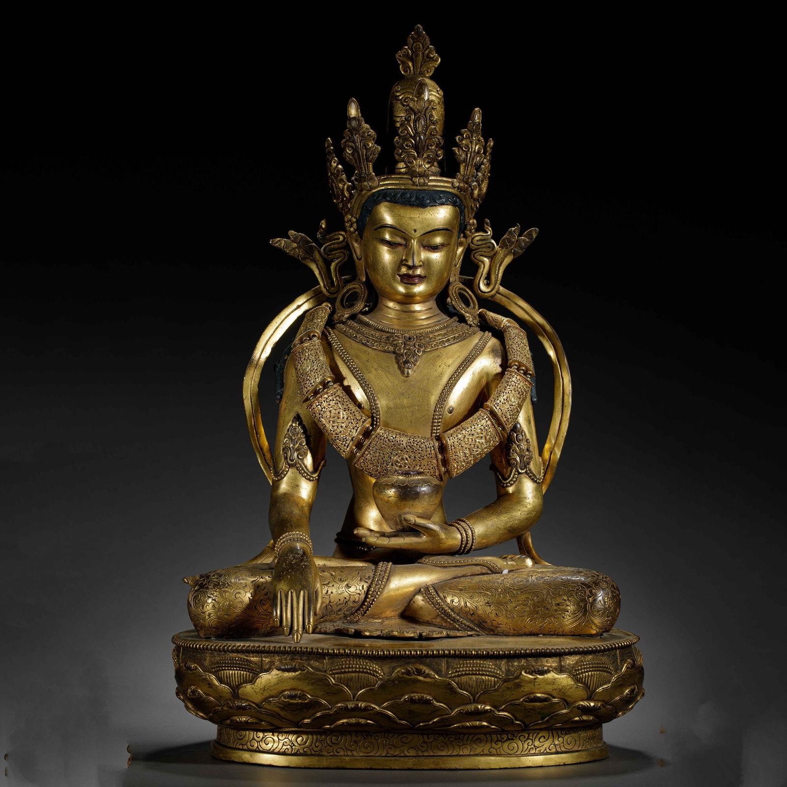 A BRONZE-GILT CROWN BUDDHA: A BRONZE-GILT CROWN BUDDHA This impressive gilt-bronze statue depicts Amitayus, the Buddha of Infinite Life, seated in dhyanasana on a double-lotus base. The figure is adorned with an elaborate