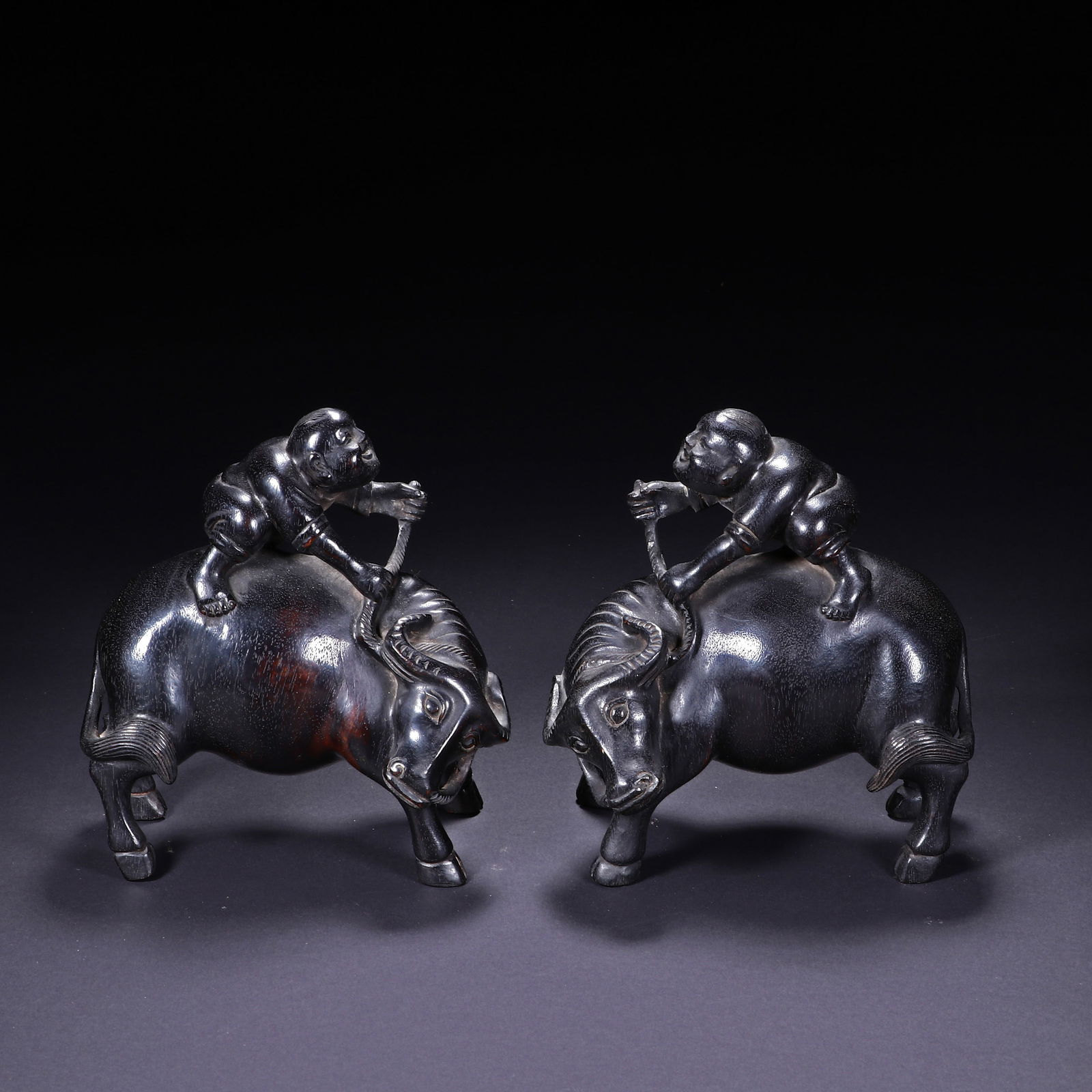 PAIR CARVED ROSEWOOD ZITAN BOY ON BUFFALOS: PAIR CARVED ROSEWOOD ZITAN BOY ON BUFFALOS This charming pair of Chinese figures is masterfully carved from dense zitan wood, depicting two plump boys riding robust buffaloes. Each boy holds a rope,