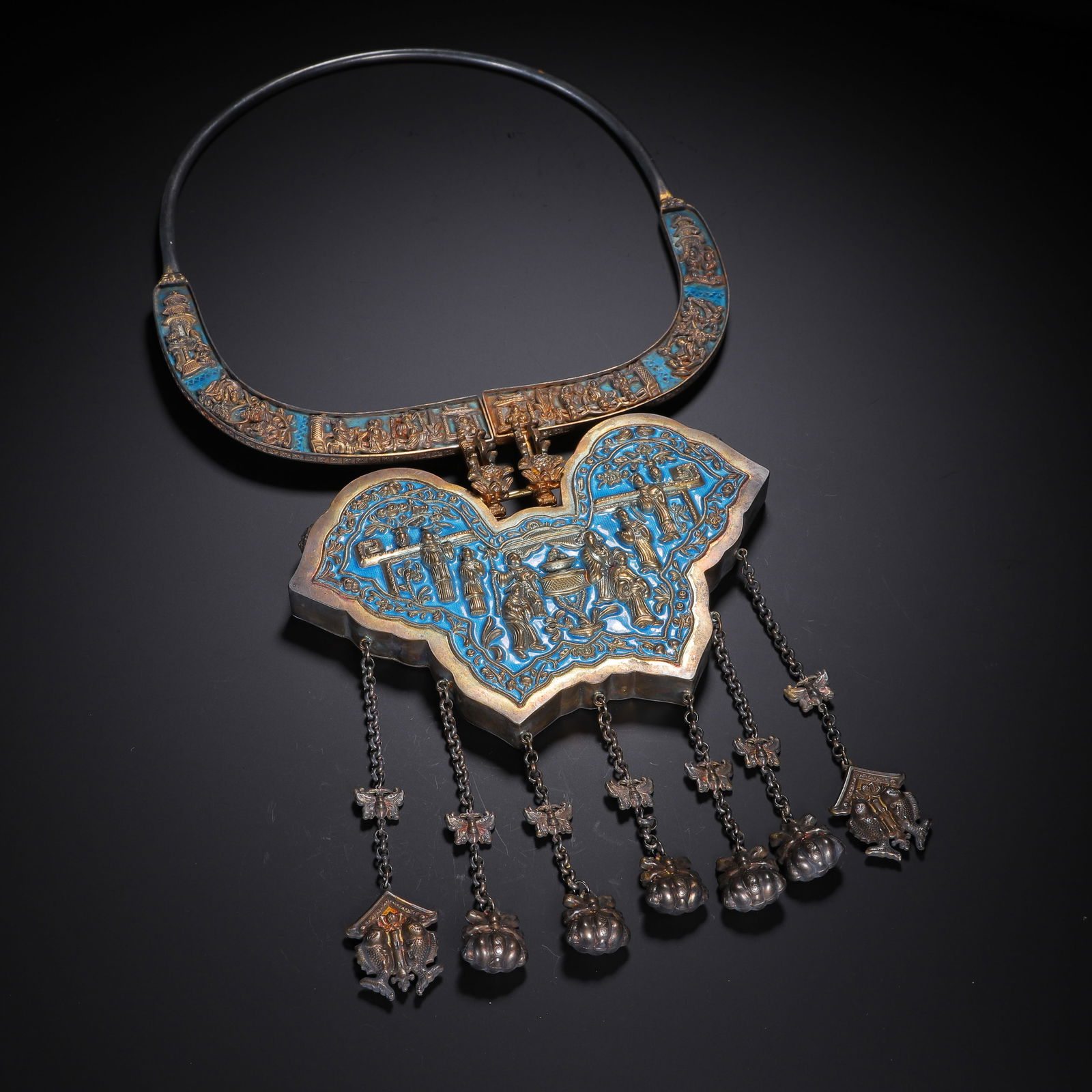 AN ENAMELED SILVER NECKLACE: AN ENAMELED SILVER NECKLACE This substantial lock pendant is crafted from silver, featuring a rectangular form with a curved top, adorned with intricate gilt-inlaid scenes of figures, horses, and