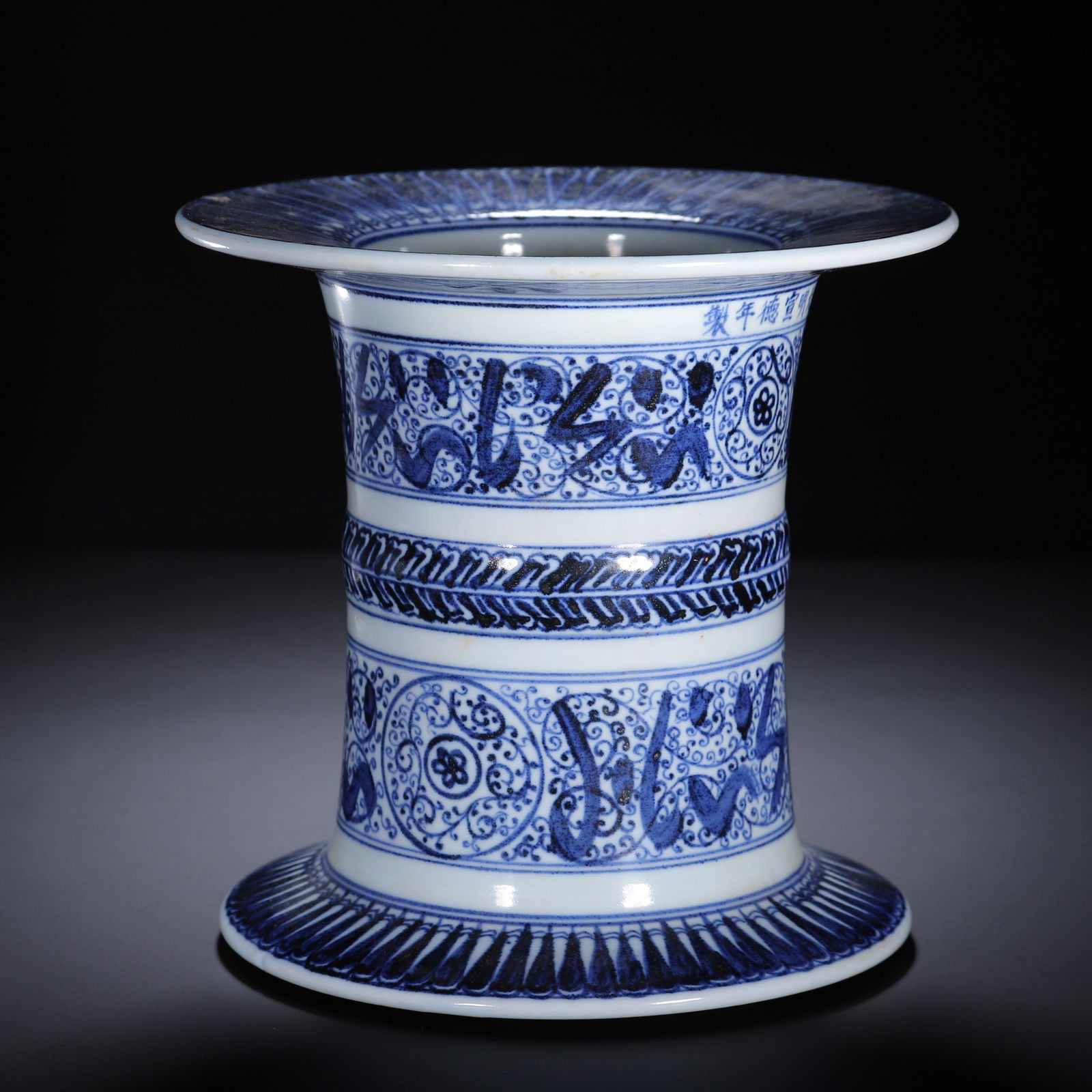 A BLUE AND WHITE VESSEL: A BLUE AND WHITE VESSEL A Chinese blue and white porcelain vase, with a flared rim, waisted body, and splayed foot. The white ground is decorated with bold blue bands of Arabic calligraphy, scrolling