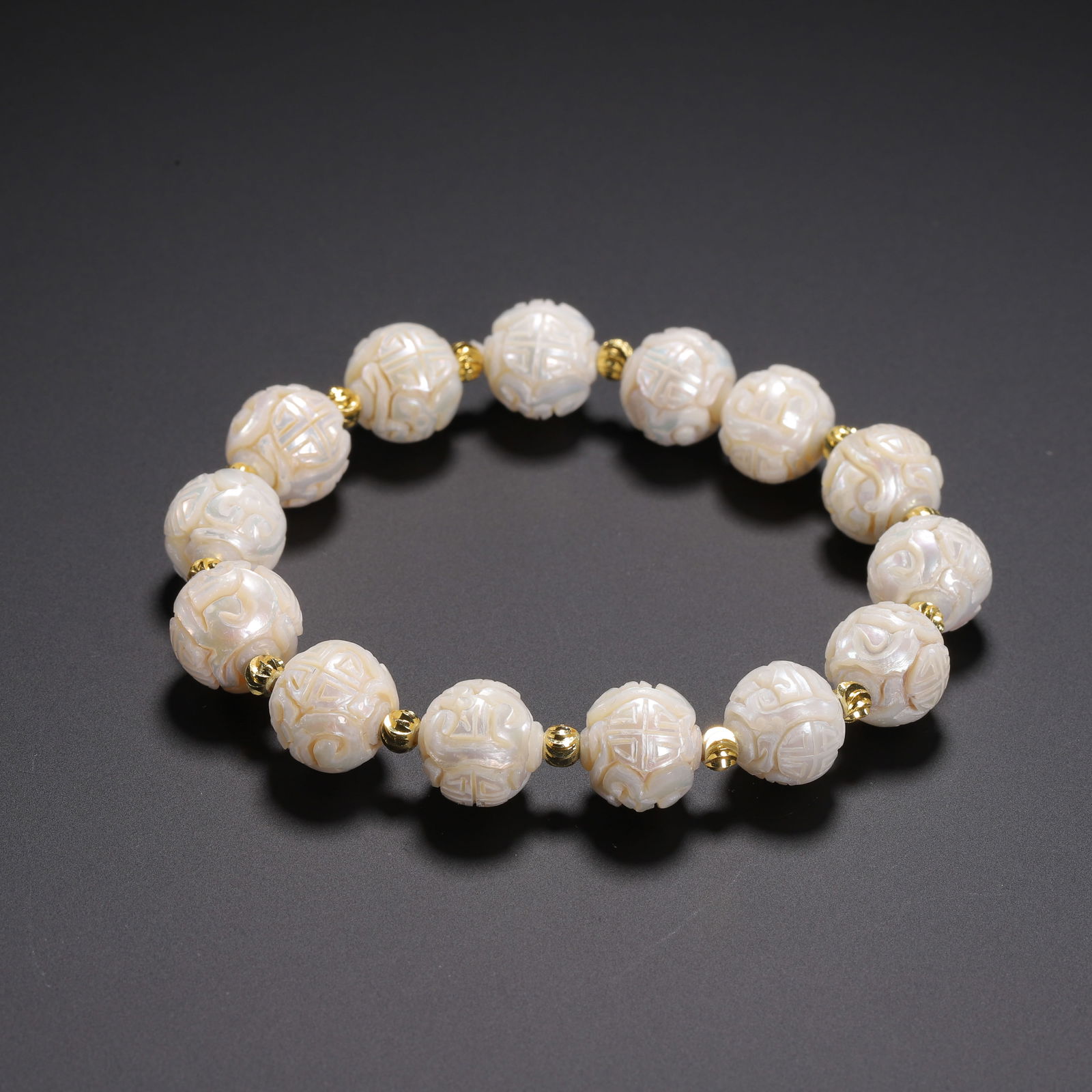 A CARVED PEARL BRACELET: A CARVED PEARL BRACELET This elegant bracelet is strung with fourteen carved Dongzhu beads, each masterfully incised with the shou (longevity) character amidst scrolling clouds. The pearls exhibit a l