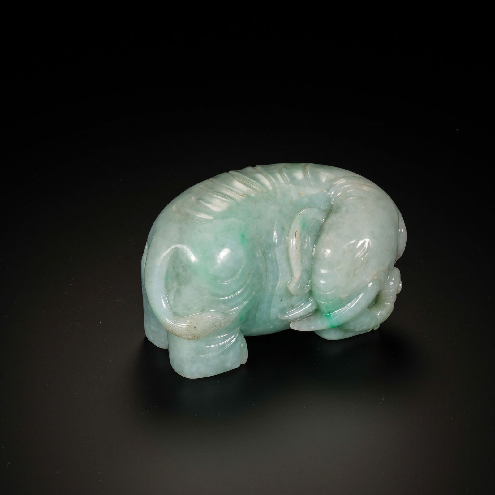 A CARVED JADEITE ELEPHANT: A CARVED JADEITE ELEPHANT A charming Chinese jadeite carving of an elephant, depicted in a recumbent pose with its trunk curled gently, embodying the classic "Taiping You Xiang" (Peace and