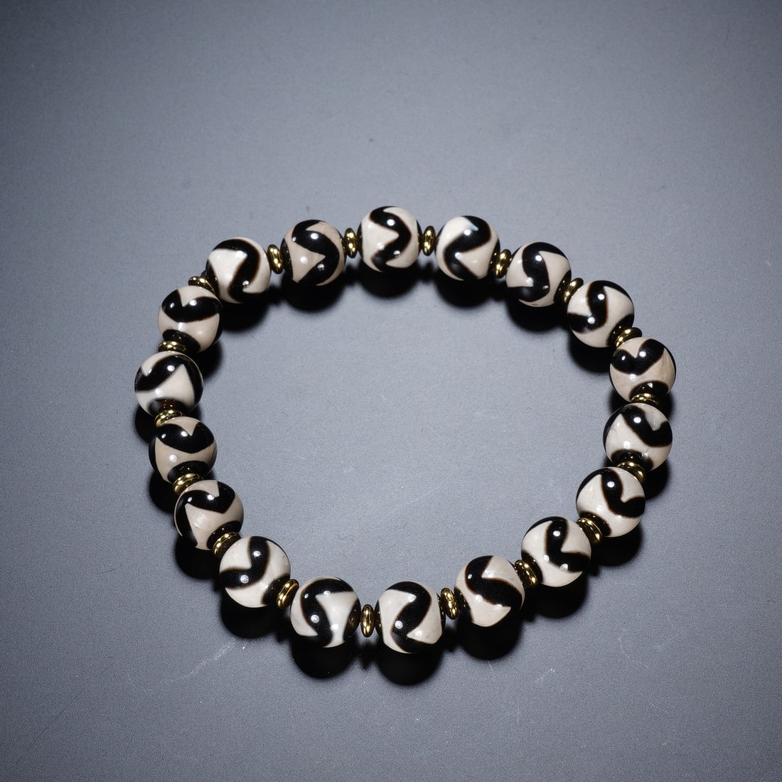 Chinese Antique Dzi Bead Bracelet: Chinese Antique Dzi Bead Bracelet This bracelet is composed of round dzi beads, each featuring distinct black ?tiger tooth? patterns on an off-white background, separated by small brass spacer beads. 
