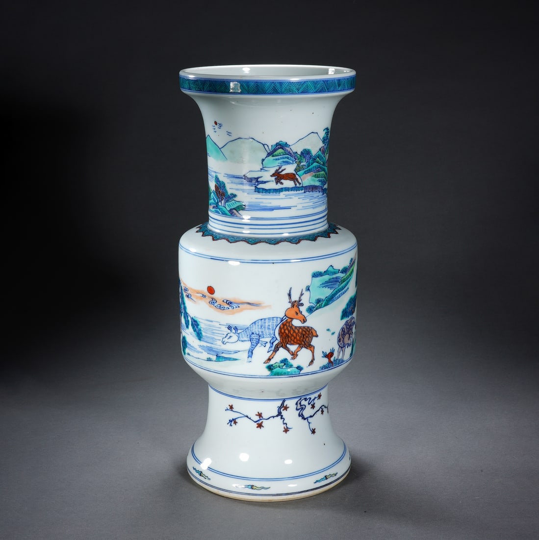 Chinese Wucai Gu-Form Vase: Chinese Wucai Gu-Form Vase This elegant Chinese porcelain gu vase is painted in the vibrant wucai palette, featuring detailed scenes of deer and other animals set within a mountainous landscape. The n