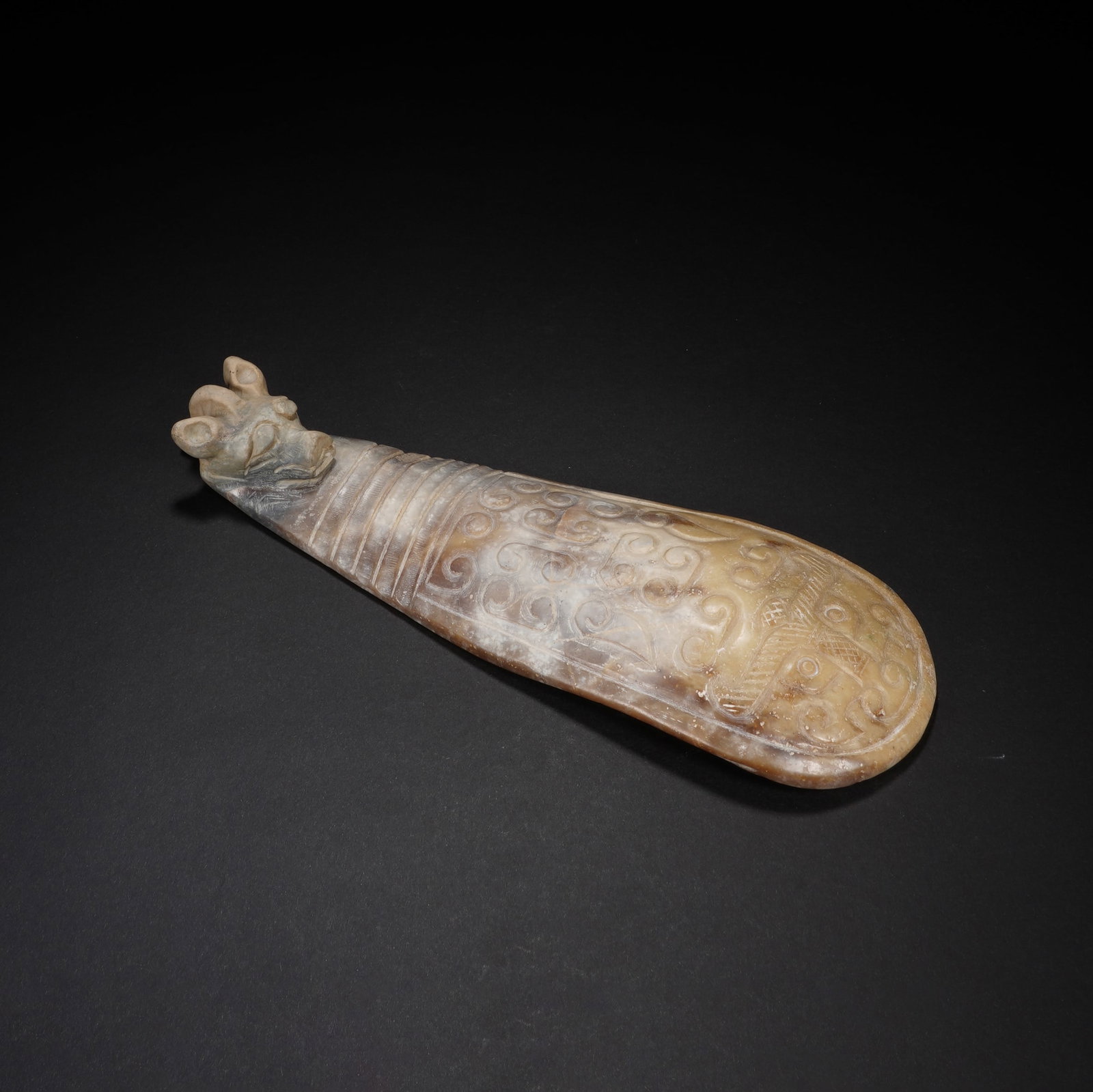 Chinese Archaistic Jade Belt Hook: Chinese Archaistic Jade Belt Hook This ancient jade belt hook is carved from a single piece of jade, showcasing a warm earthy patina with age-related calcification. The hook is finely sculpted into a 