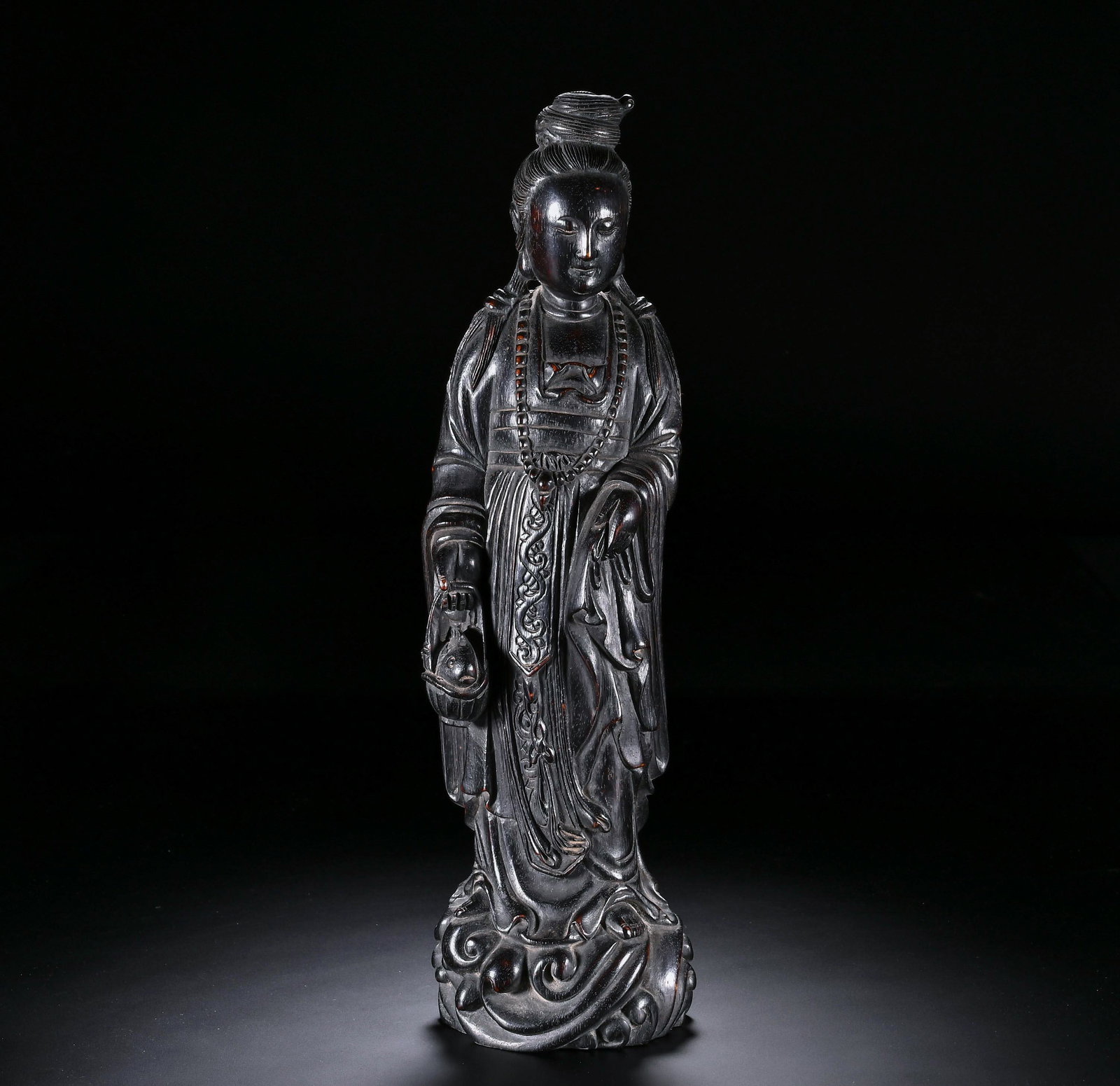 A Chinese Zitan Wood Carving of Standing Guanyin: A Chinese Zitan Wood Carving of Standing Guanyin This elegant standing Guanyin carving, measuring 27.5 cm in height and 7.5 cm in width, is masterfully crafted from solid zitan wood. The figure is dep