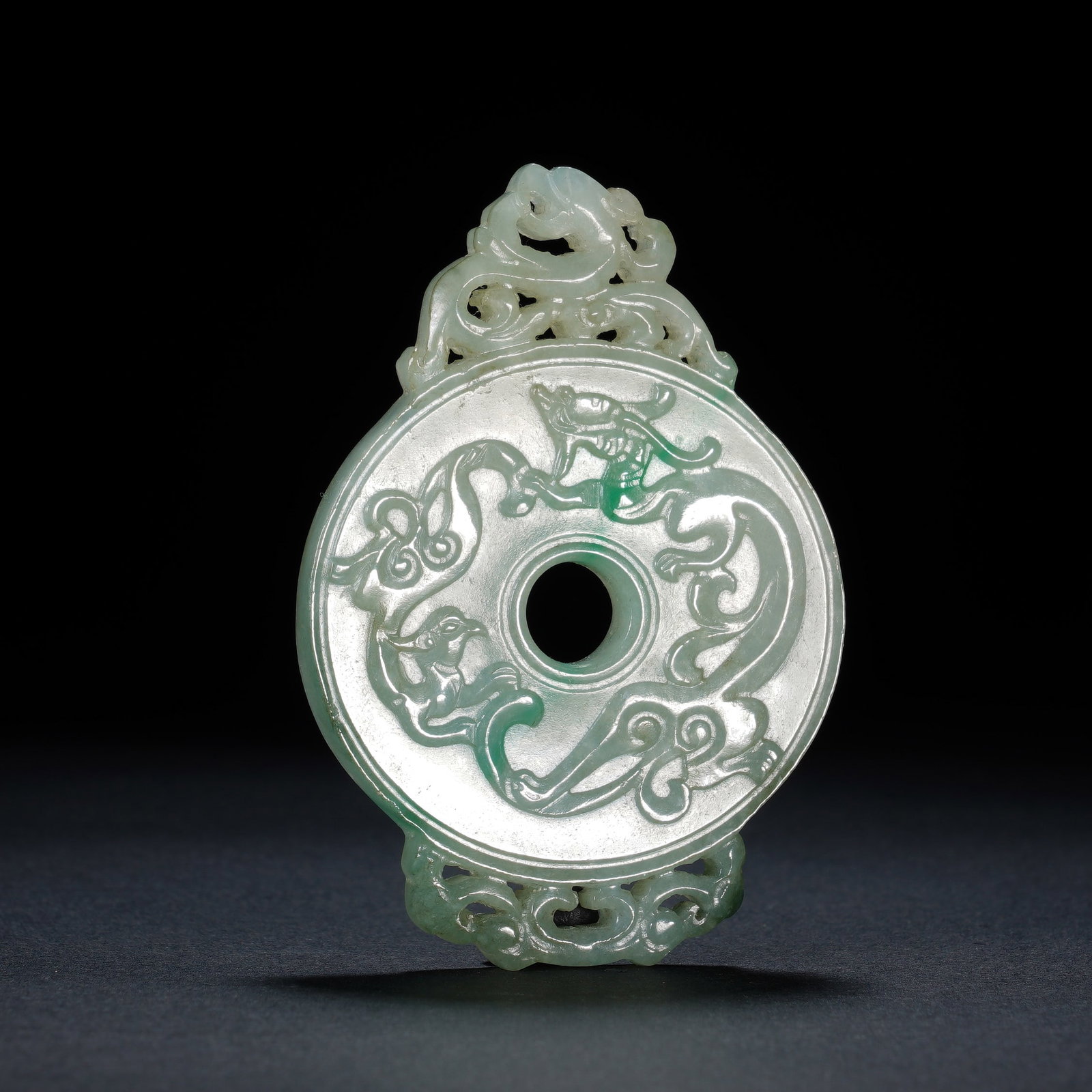 A CHINESE JADEITE CHILONG BI PENDANT: A CHINESE JADEITE CHILONG BI PENDANT This pierced jadeite bi pendant measures 4.5 cm wide, 6.6 cm tall with a thickness of 0.6 cm, weighing 35 grams. Crafted from translucent pale celadon jadeite with