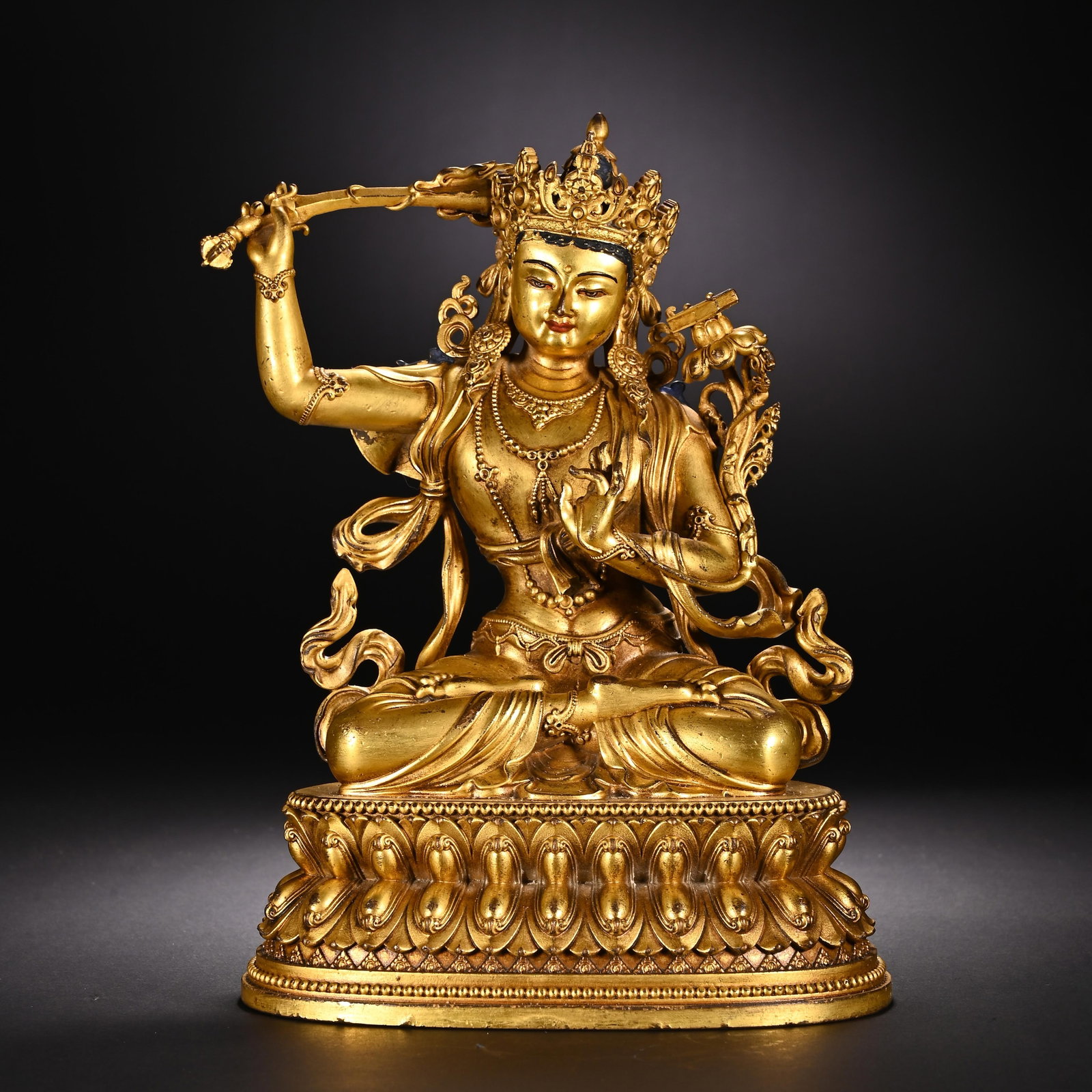 A CHINESE GILT BRONZE MANJUSHRI BODHISATTVA STATUE: A CHINESE GILT BRONZE MANJUSHRI BODHISATTVA STATUE This fully gilt bronze Manjushri, the Bodhisattva of wisdom, is seated in full lotus posture on a double lotus pedestal edged with delicate beaded bo