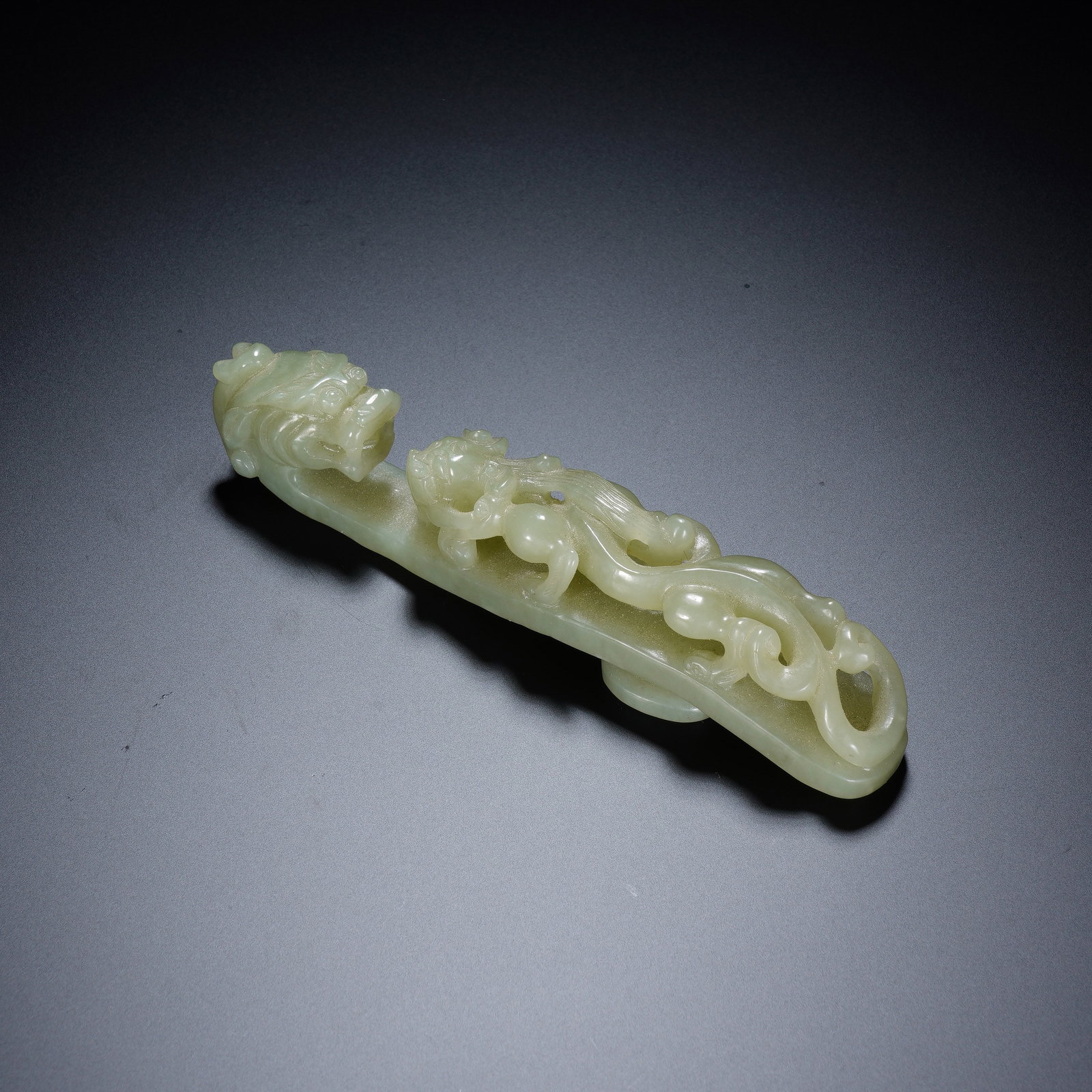 A CHINESE WHITE JADE DRAGON BELT HOOK: A CHINESE WHITE JADE DRAGON BELT HOOK This nephrite belt hook measures 11.3 cm long, 2 cm wide and 2.5 cm tall, weighing 64 grams. The terminal head is finely carved as a robust dragon head with defin