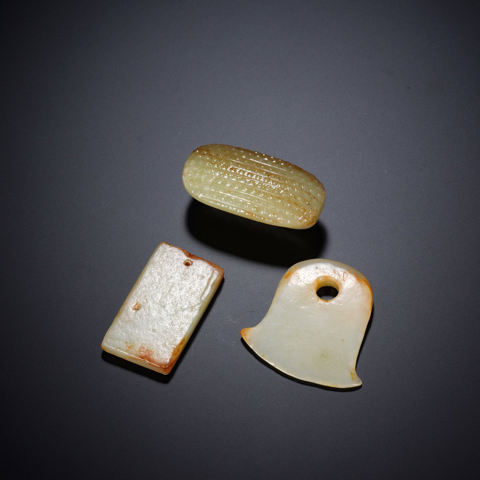 A GROUP OF THREE CHINESE ARCHAIC JADE ORNAMENTS: A GROUP OF THREE CHINESE ARCHAIC JADE ORNAMENTS This ensemble contains three distinct nephrite ornaments measuring respectively 4.5?4.5?0.7 cm, 2.7?4.6?0.6 cm and 5.3?2.8?2.2 cm, with an aggregate wei