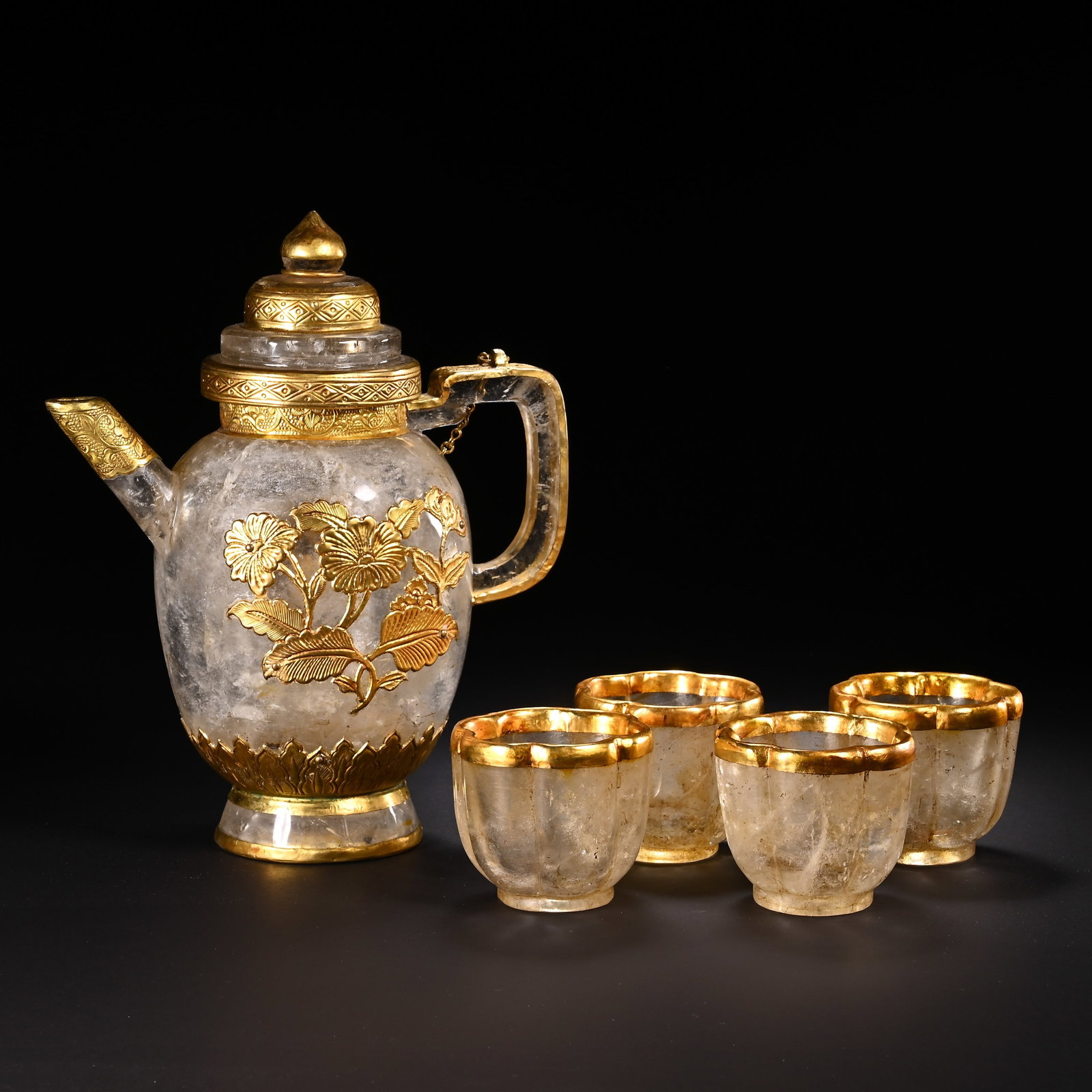 A SET OF CHINESE GILDED ROCK CRYSTAL WINE VESSELS: A SET OF CHINESE GILDED ROCK CRYSTAL WINE VESSELS This complete wine service set comprises one rock crystal ewer paired with four matching cups, all embellished with polished gilded mounts. The transl