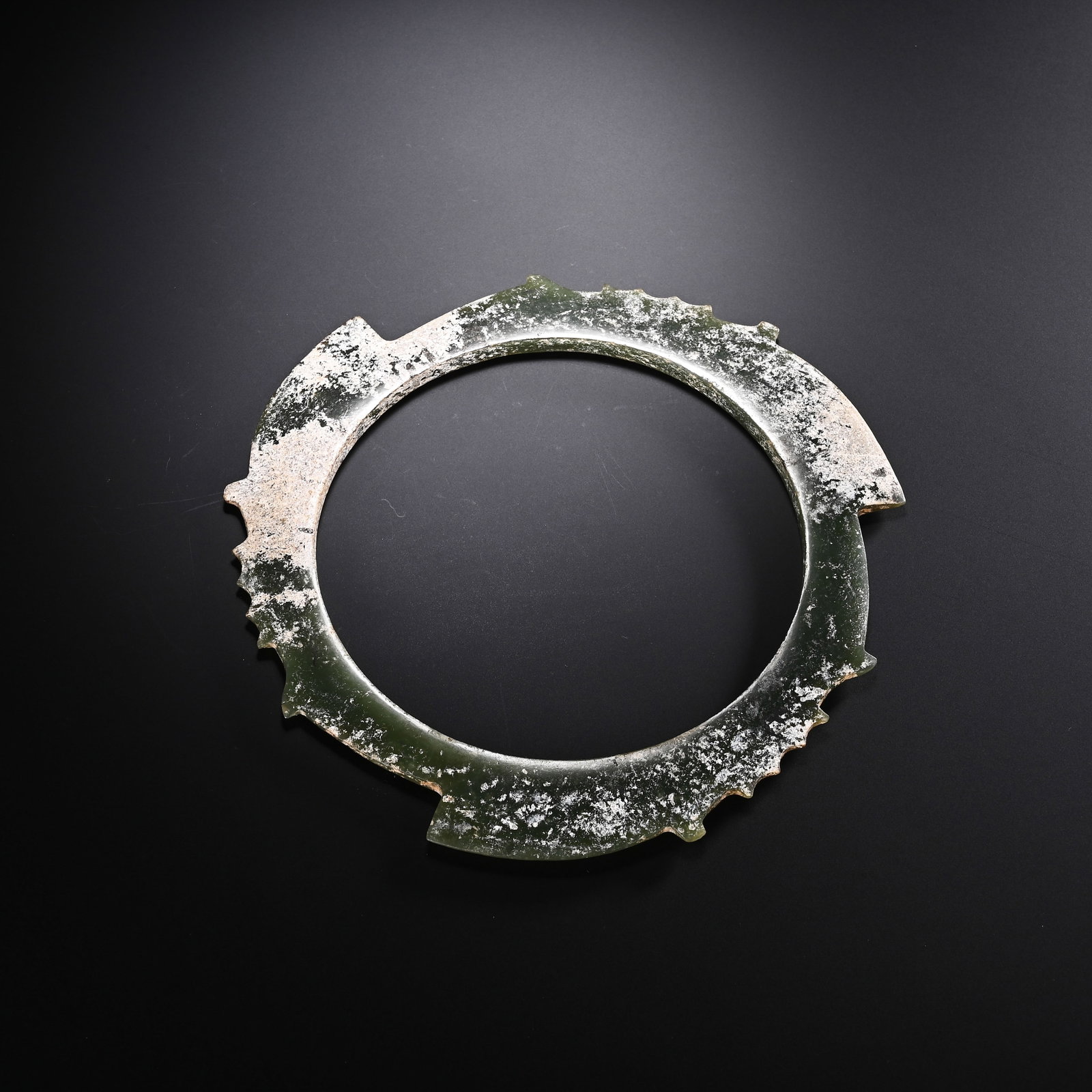A CHINESE ARCHAIC JADE XUANJI ASTRONOMICAL RING: A CHINESE ARCHAIC JADE XUANJI ASTRONOMICAL RING Carved from deep spinach-green jade, this circular xuanji astronomical ring features regularly spaced serrated notches protruding along its outer rim,