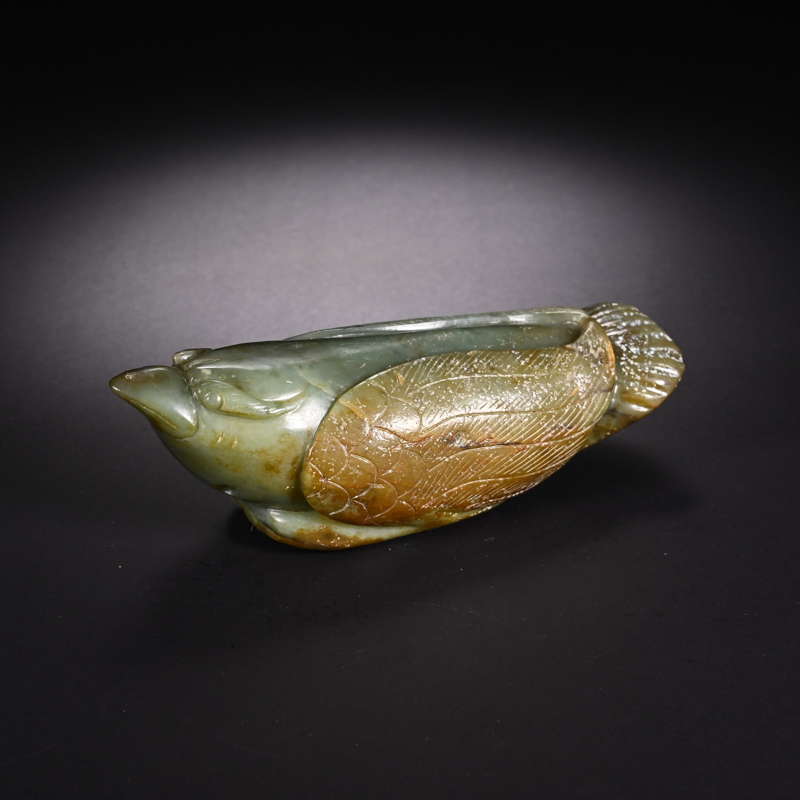 A CHINESE CELADON JADE BIRD-FORM HAND TOGGLE: A CHINESE CELADON JADE BIRD-FORM HAND TOGGLE This handheld ornament is fully carved as a plump resting bird from celadon nephrite jade naturally streaked with russet and ochre skin patina across its w