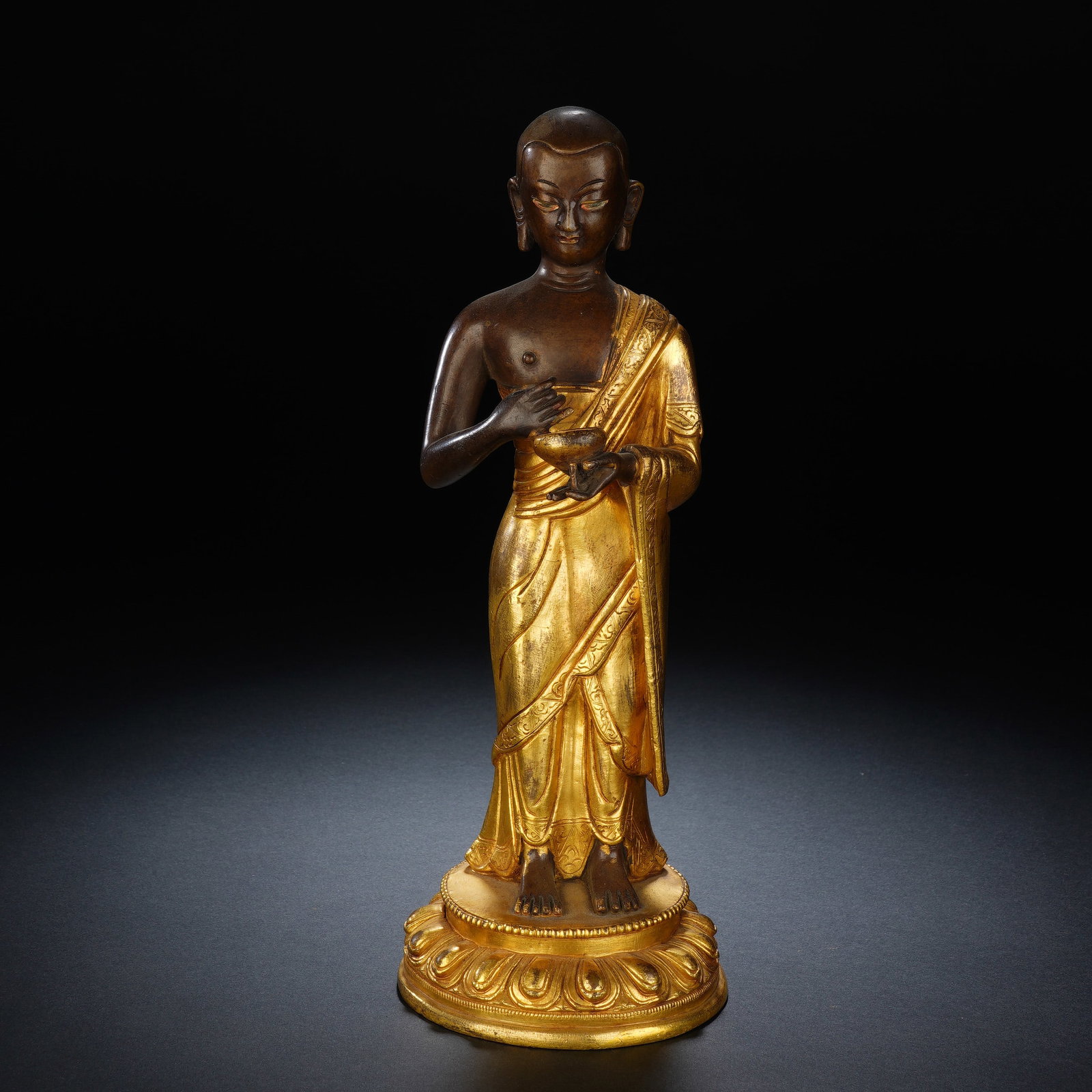A CHINESE GILT BRONZE STANDING ARHAT STATUE: A CHINESE GILT BRONZE STANDING ARHAT STATUE This standing gilt bronze arhat figure measures 8.3 cm wide, 8 cm deep and 22 cm tall, weighing 920 grams. The monk stands upright atop a fully gilded tiere