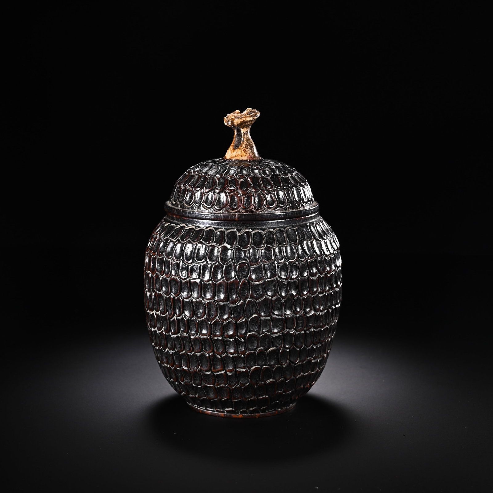 A CHINESE ZITAN WOOD TEA CADDY: A CHINESE ZITAN WOOD TEA CADDY Crafted from dense, dark zitan hardwood, this ovoid tea storage jar is entirely covered in deeply carved overlapping scale texture that wraps seamlessly across the body 