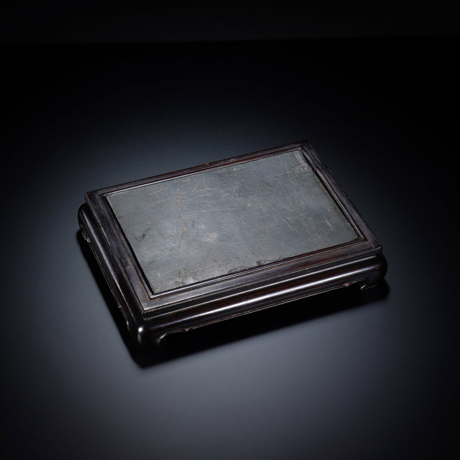 A CHINESE ZITAN FRAMED INKSTONE: A CHINESE ZITAN FRAMED INKSTONE This rectangular inkstone measures 18cm ? 13cm ? 3.5cm, featuring a smooth dark inkstone panel inset within a solid zitan hardwood frame. The stone surface bears fine n