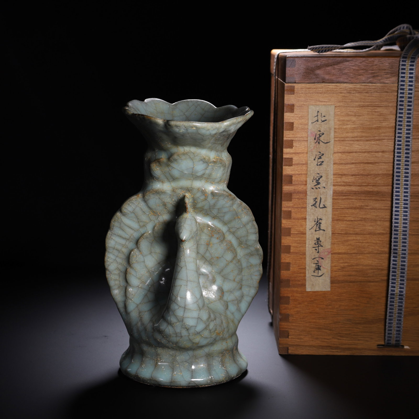 A CHINESE GUAN WARE PEACOCK VASE: A CHINESE GUAN WARE PEACOCK VASE A uniquely modelled vase entirely enveloped in pale celadon Guan glaze covered with characteristic dense crackle veins. The vessel is sculpted in the form of a standin