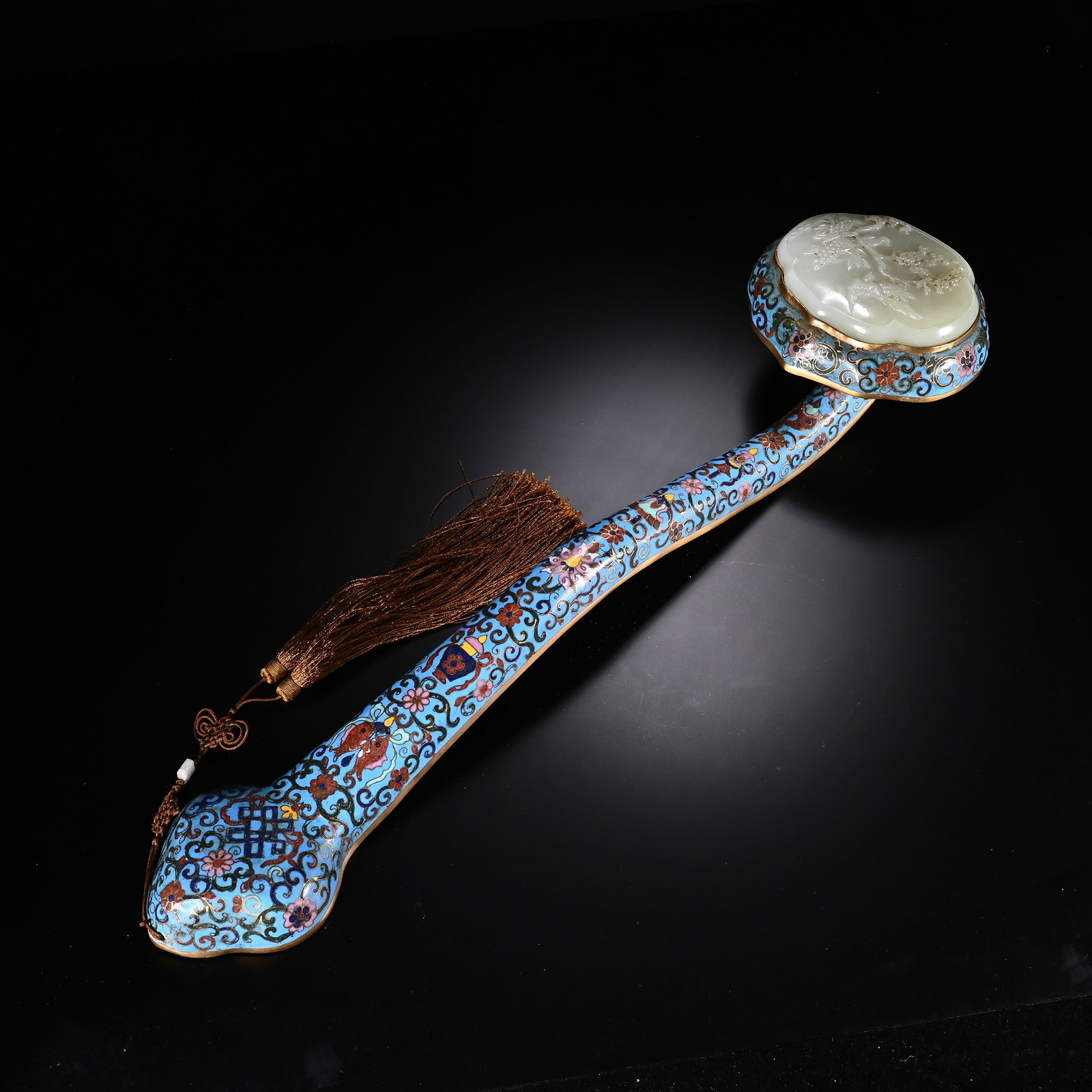 A CHINESE CLOISONNE RUYI SCEPTER INLAID WITH WHITE NEPHRITE JADE: A CHINESE CLOISONNE RUYI SCEPTER INLAID WITH WHITE NEPHRITE JADE This ceremonial ruyi sceptre is crafted from gilded copper with elaborate cloisonn? enamel work across its curved shaft and terminal he
