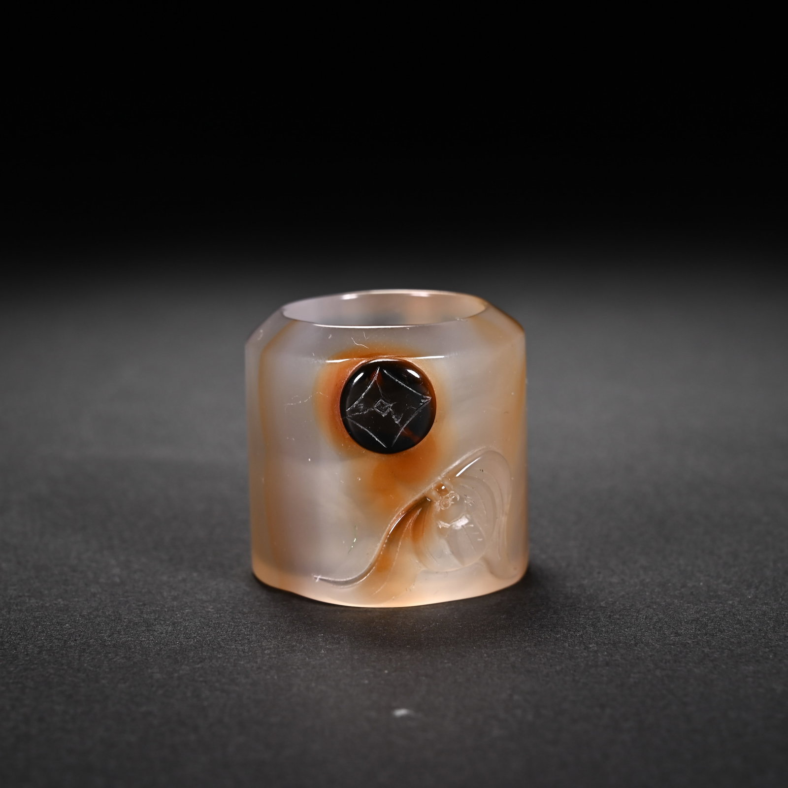 A CHINESE AGATE BAT AND COIN ARCHER'S RING: A CHINESE AGATE BAT AND COIN ARCHER'S RING This hexagonal archer's thumb ring is polished from translucent pale agate naturally streaked with warm amber russet hues. Leveraging a distinct dark natural