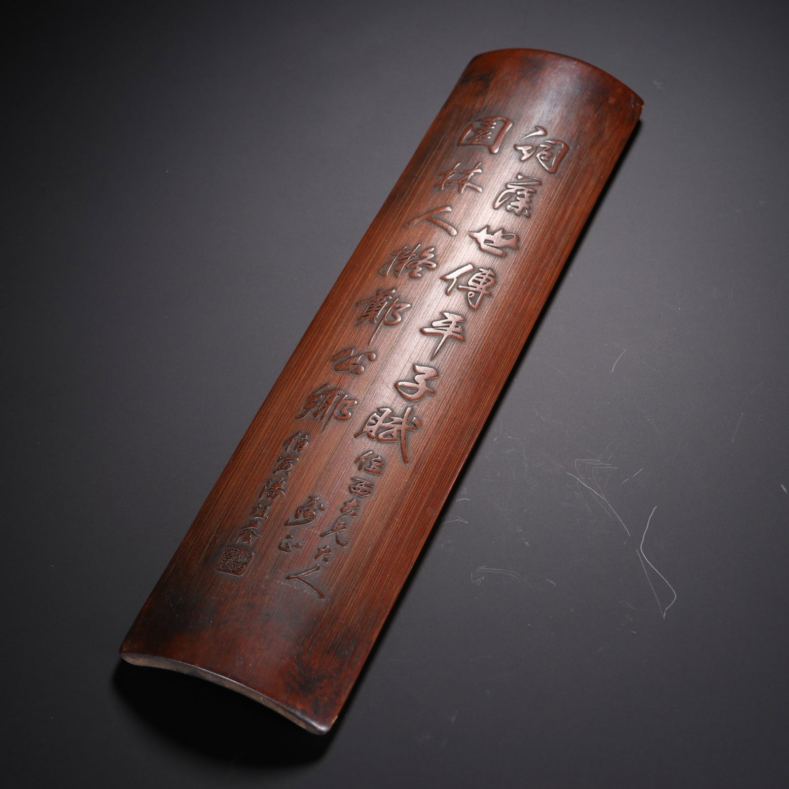 A CHINESE CARVED BAMBOO WRIST REST WITH CALLIGRAPHIC VERSE: A CHINESE CARVED BAMBOO WRIST REST WITH CALLIGRAPHIC VERSE This literati arm guard measures 27cm long, 6.6cm wide and weighs 97.8 grams, formed from aged bamboo with a rich warm reddish-brown patina. 