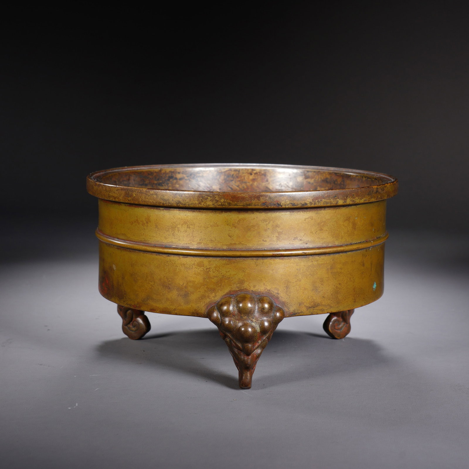 A CHINESE TRIPOD BRONZE CENSER: A CHINESE TRIPOD BRONZE CENSER This cylindrical bronze censer measures 14 cm in diameter and 8 cm in height, weighing 1159 grams. The smooth rounded body is encircled by a single raised horizontal ban