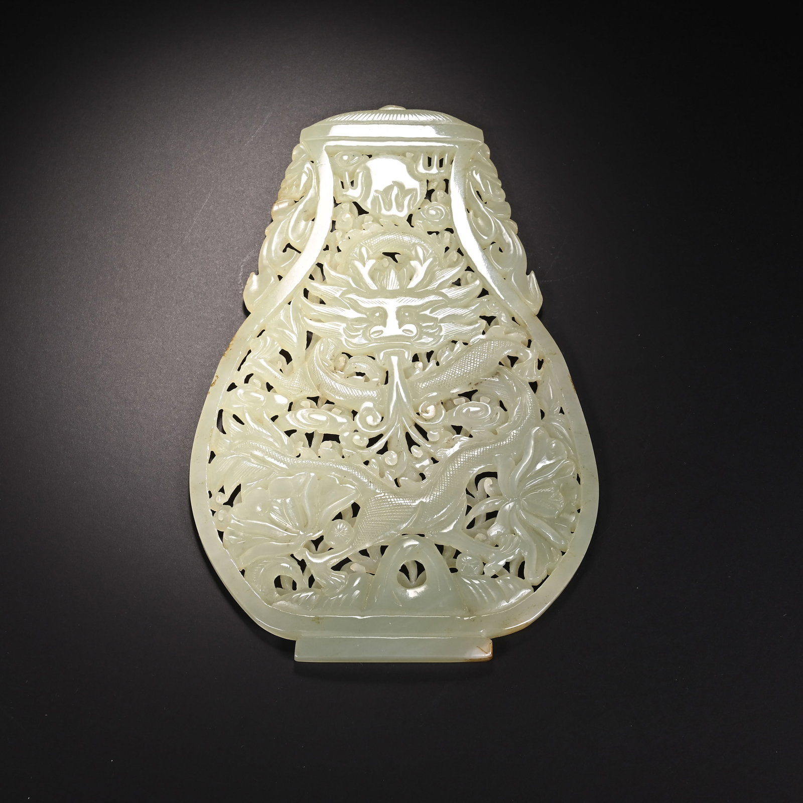 A CHINESE OPENWORK JADE TABLE SCREEN WITH DRAGON MOTIFS: A CHINESE OPENWORK JADE TABLE SCREEN WITH DRAGON MOTIFS This pear-shaped jade plaque is crafted from pale celadon nephrite jade and executed with elaborate multi-layered openwork carving. A coiled imp