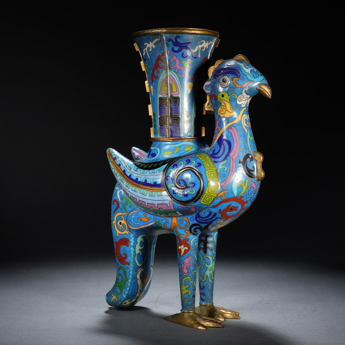 A CHINESE CLOISONNE BRONZE PHOENIX ZUN VESSEL: A CHINESE CLOISONNE BRONZE PHOENIX ZUN VESSEL Cast bronze vessel decorated with elaborate wire cloisonne enamel, modelled as a celestial phoenix standing firmly on gilded taloned feet, surmounted by a
