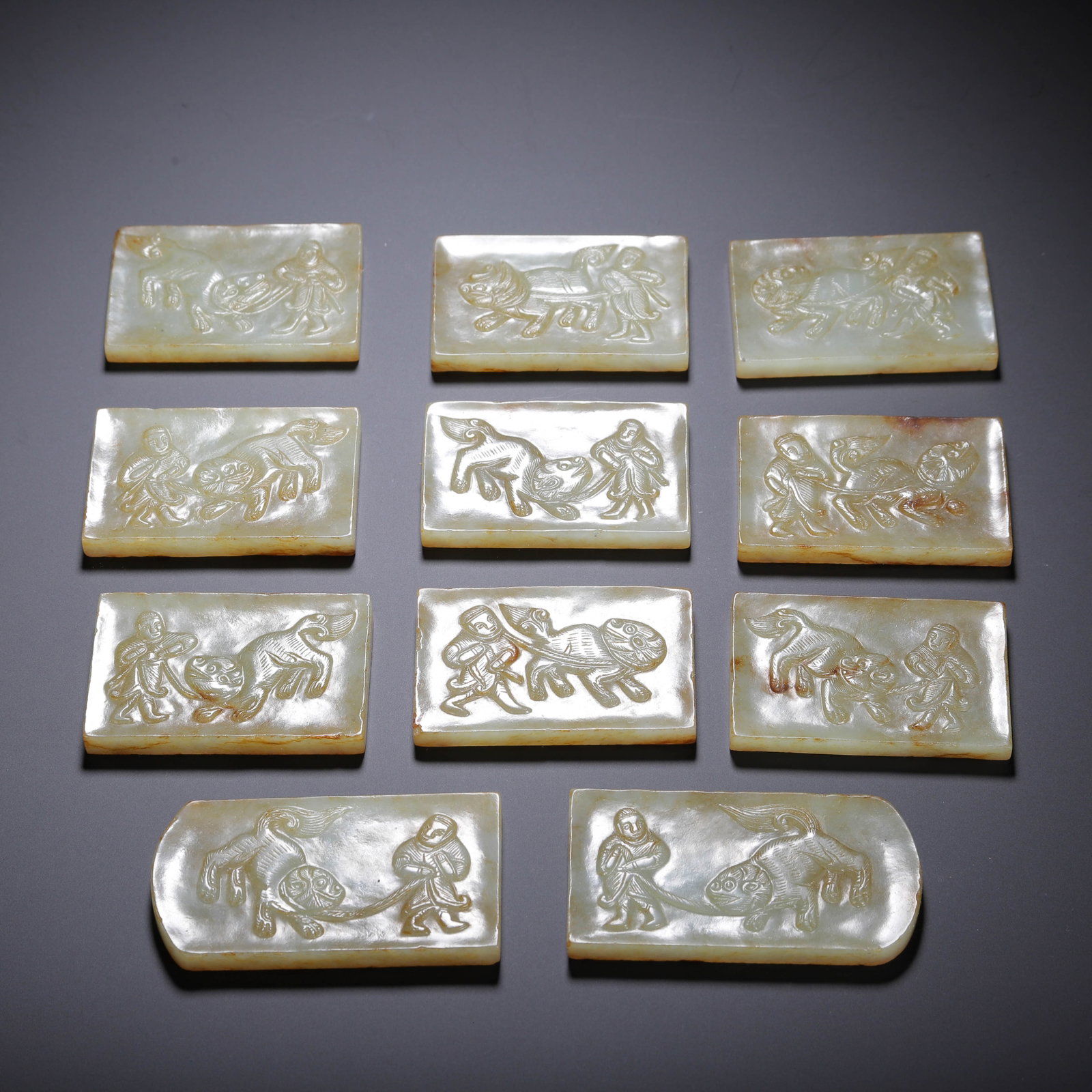 A SET OF CHINESE HETIAN JADE BELT PLAQUES: A SET OF CHINESE HETIAN JADE BELT PLAQUES A complete suite of eleven nephrite belt plaques carved from pale Hetian jade with natural warm russet inclusions across the surface. Each rectangular plaque 