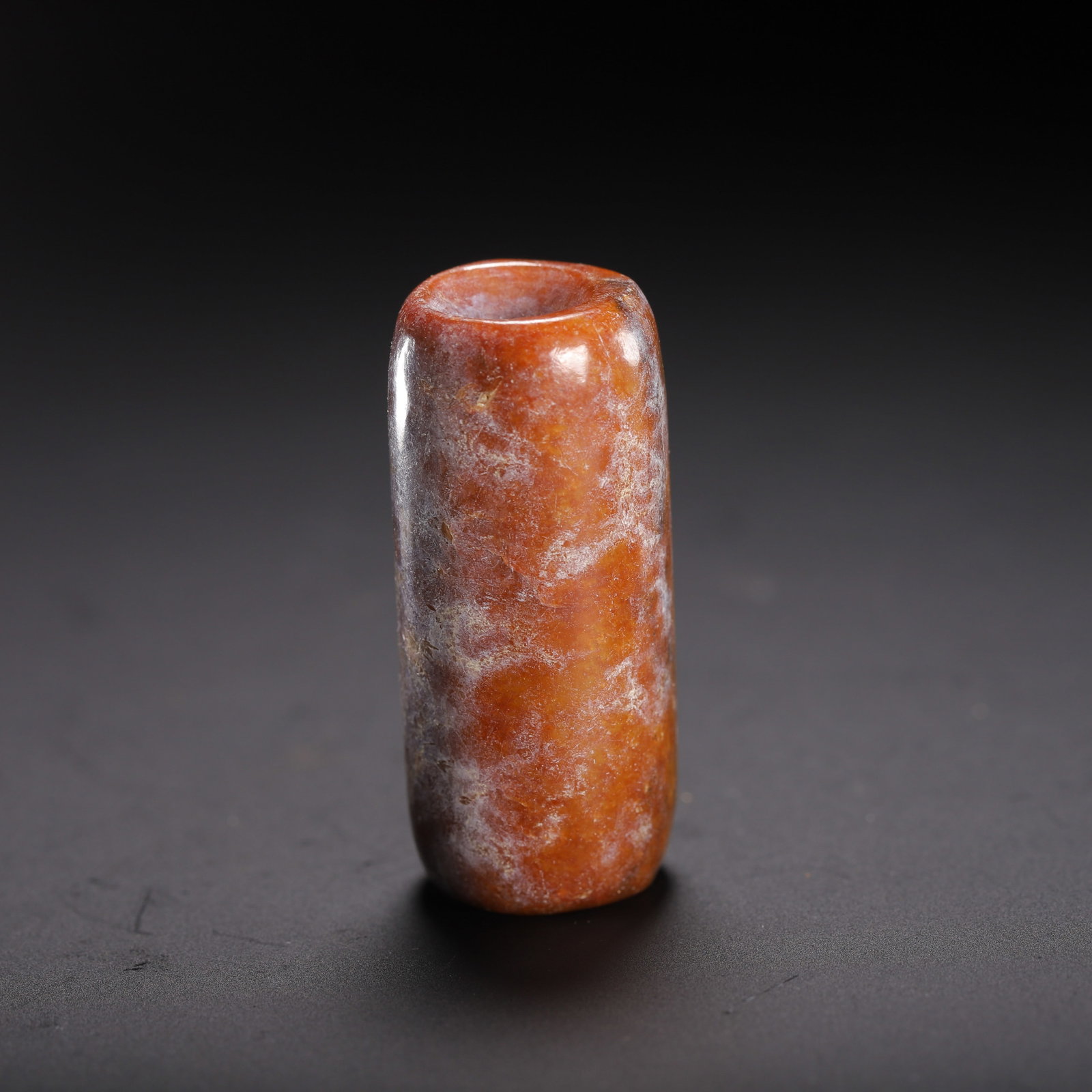 A CHINESE HETIAN JADE CYLINDRICAL TUBE PENDANT: A CHINESE HETIAN JADE CYLINDRICAL TUBE PENDANT This tubular jade bead is crafted from Hetian nephrite suffused with rich russet orange tones, overlaid with extensive milky grey ancient calcified patin
