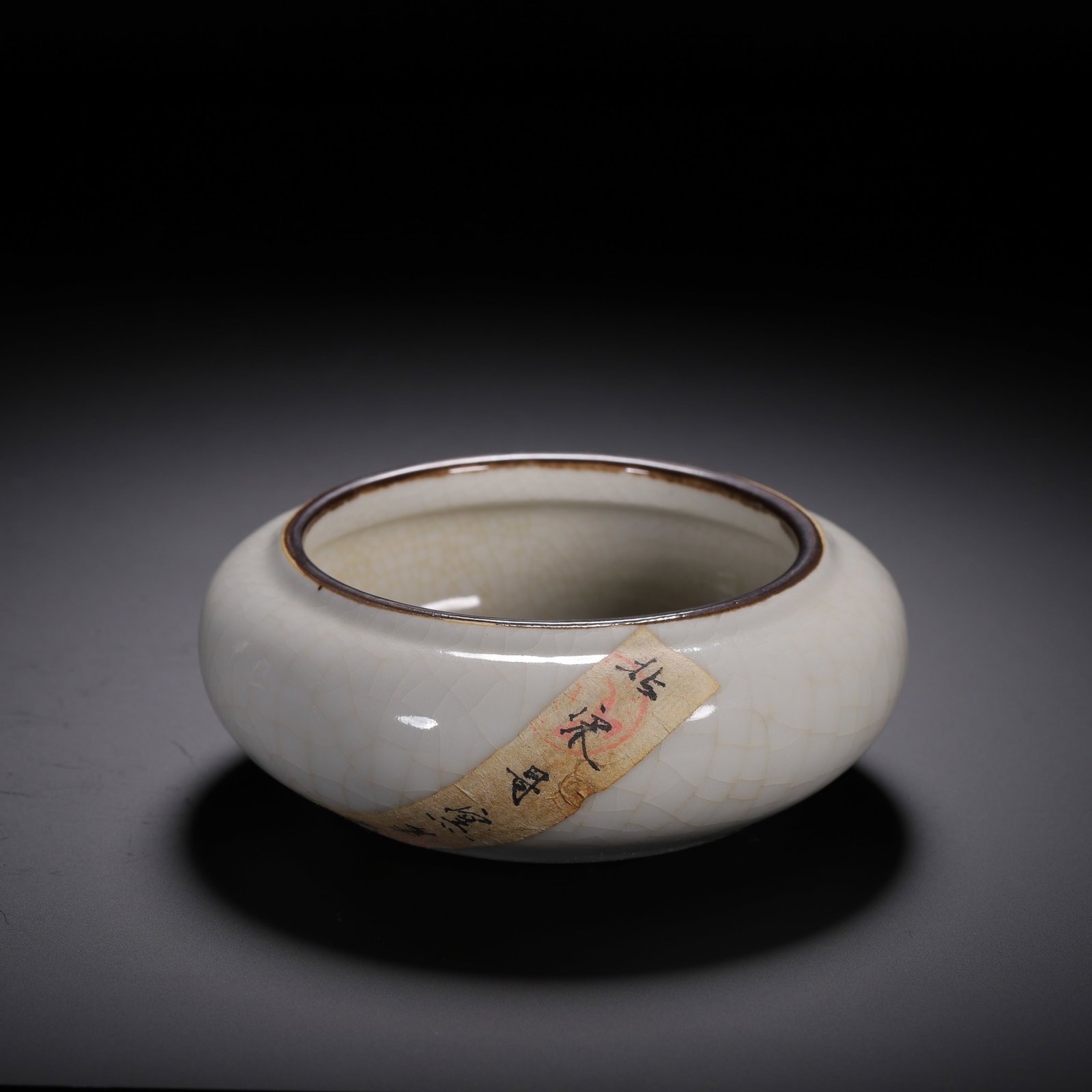 A CHINESE GE KILN CRACKLE GLAZE WATER WASHER: A CHINESE GE KILN CRACKLE GLAZE WATER WASHER A flattened globular scholar's washer with a short constricted opening trimmed by a thin dark brown metal rim. The entire interior and exterior are covered
